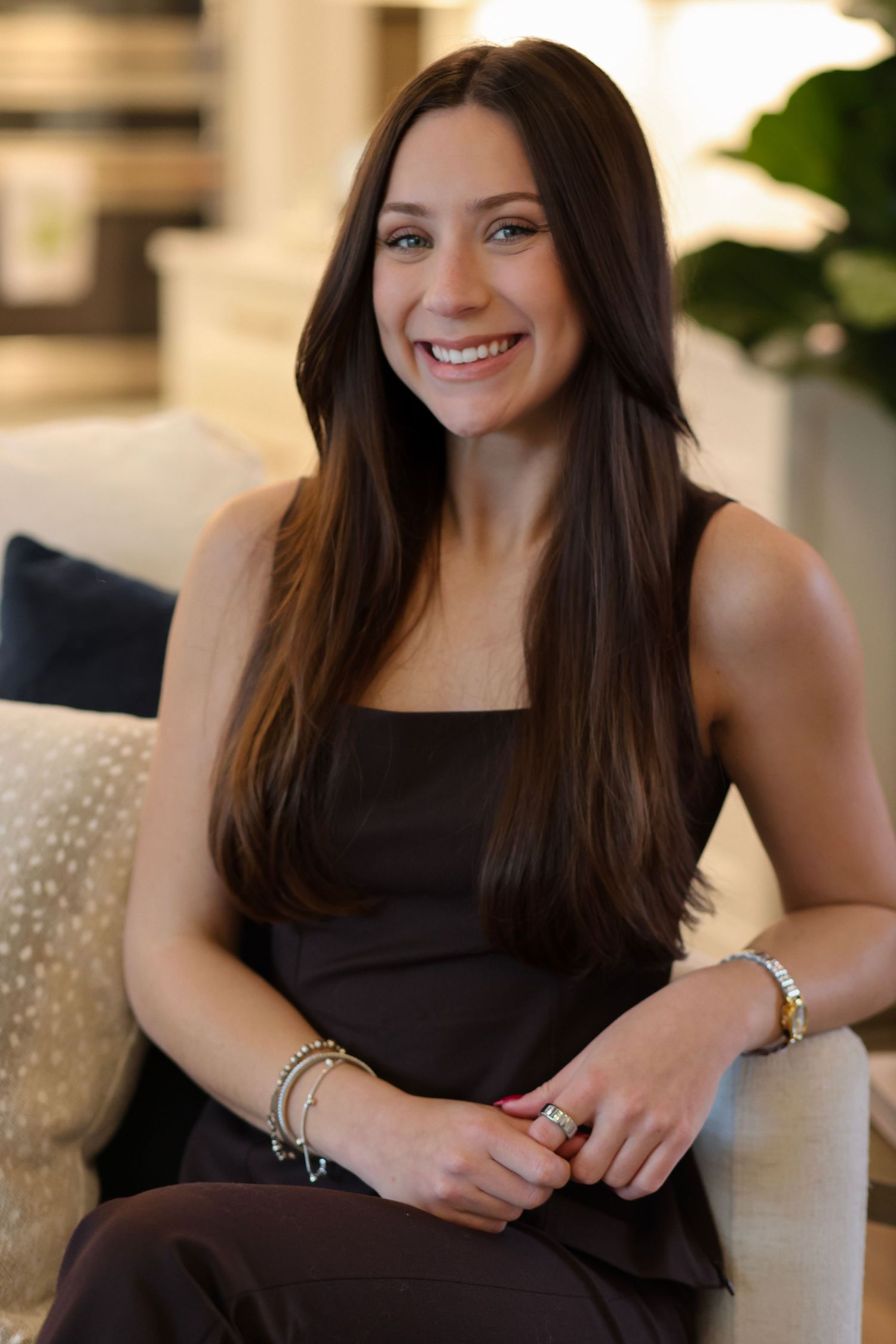 Person wearing a black sleeveless top sits casually in a modern interior setting with warm lighting.