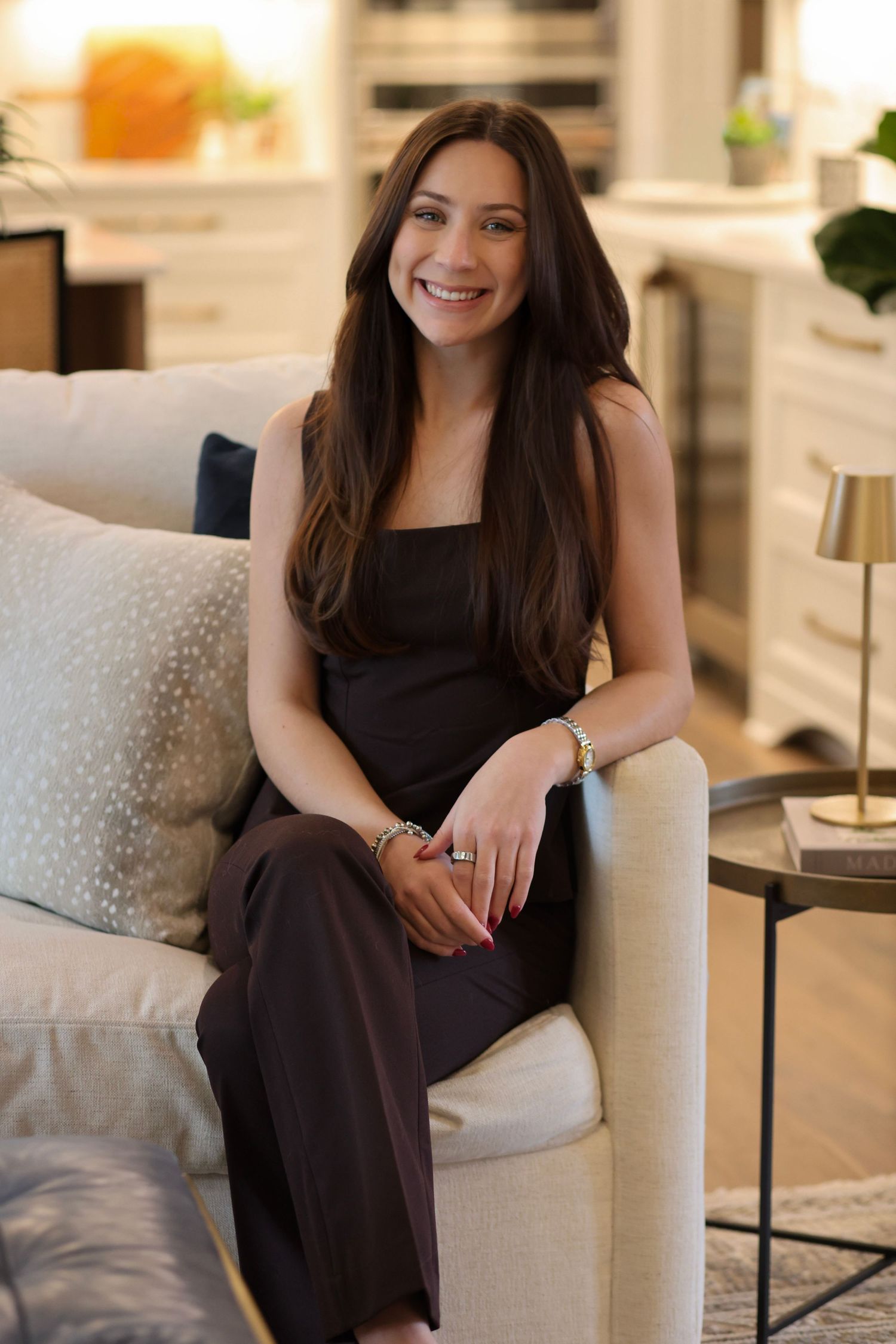 A person in a black dress sits comfortably on a white armchair in an elegant interior setting.