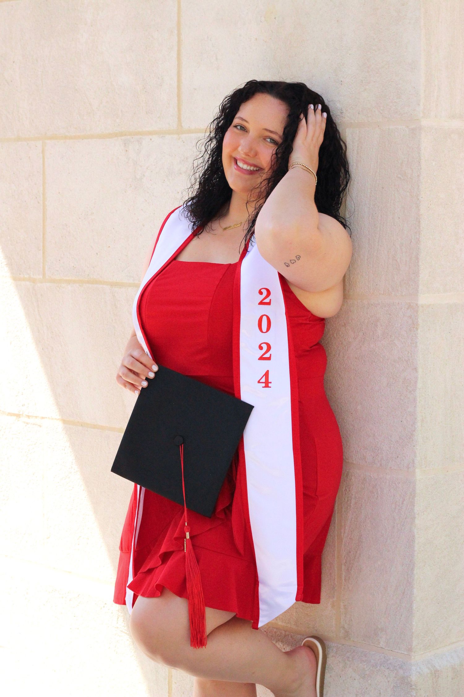 Graduate wearing red dress and white stole poses with graduation cap.