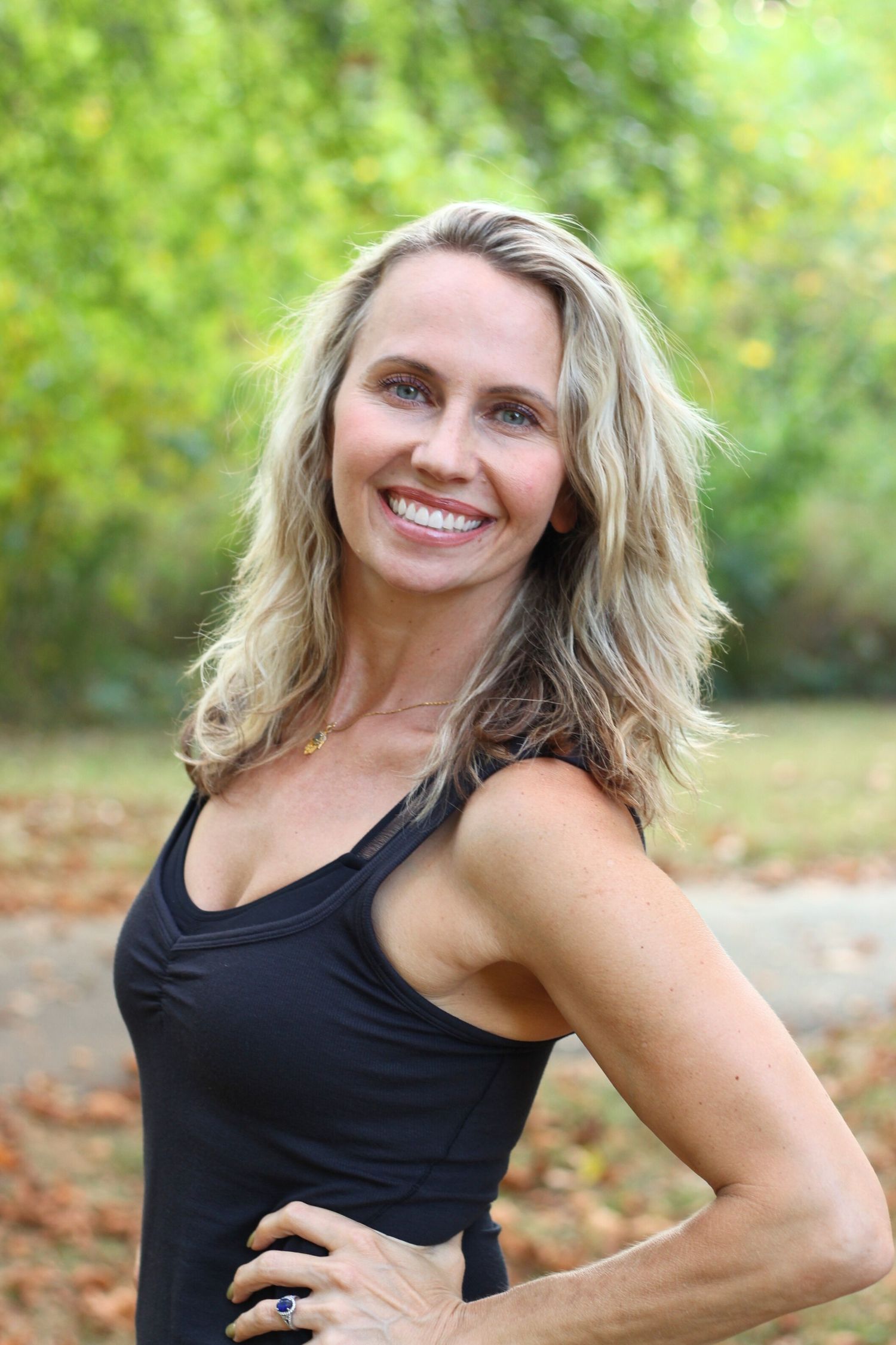 Athletic figure in black tank top poses outdoors during fitness photoshoot.