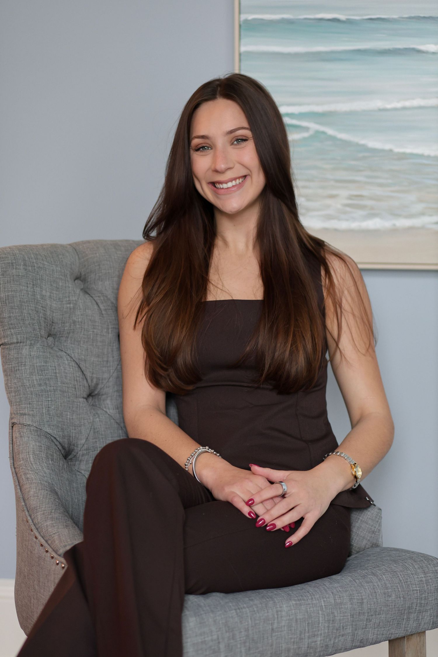 Woman relaxing on tufted gray sofa with beach artwork and modern decor in background.