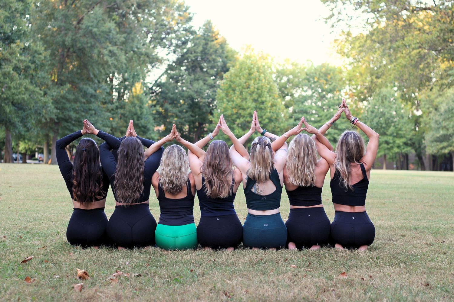 Group of people sitting in a row showing their hair cascading down their backs outdoors.
