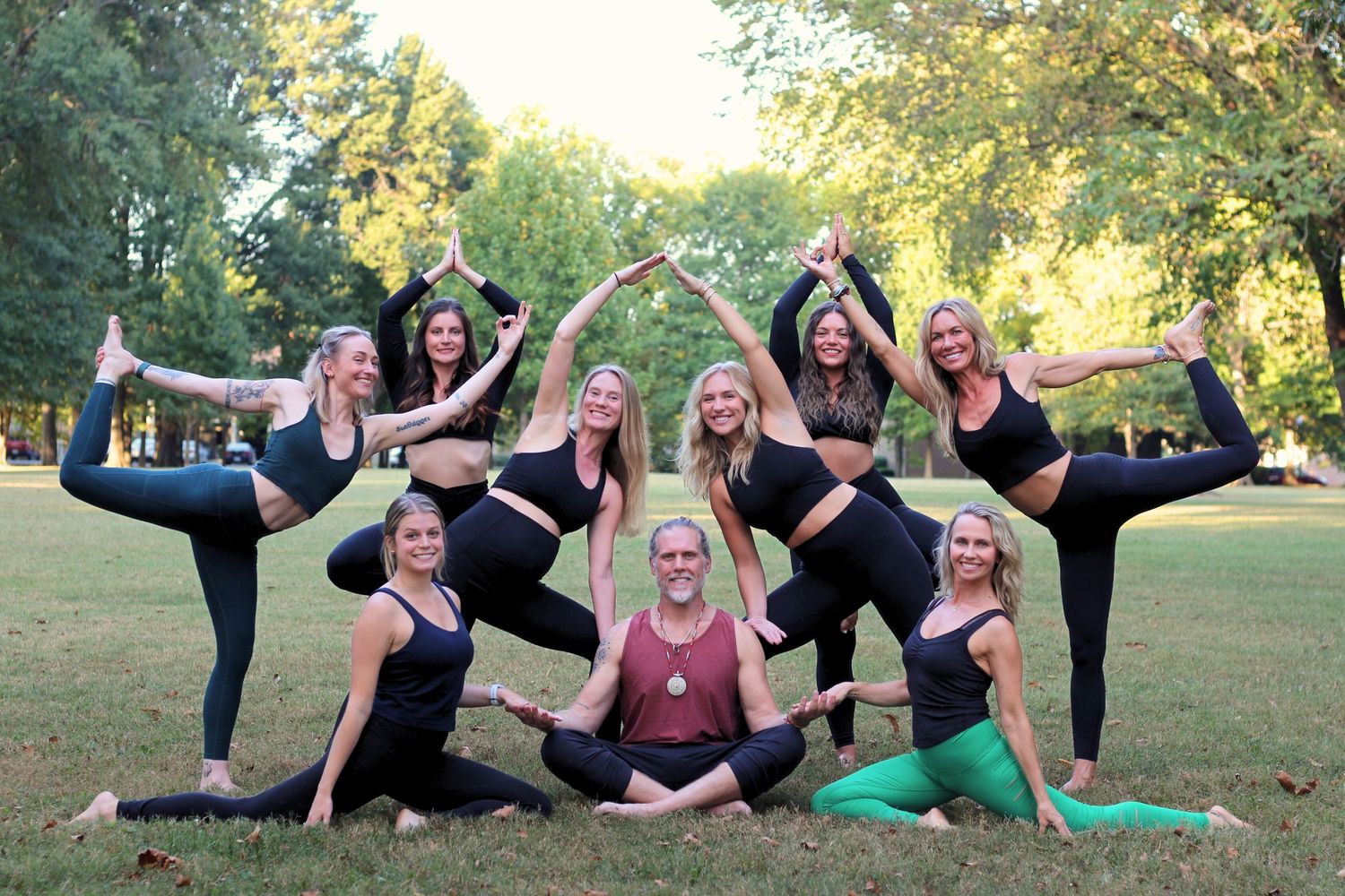 Group of people in black outfits strike playful yoga poses on grass.