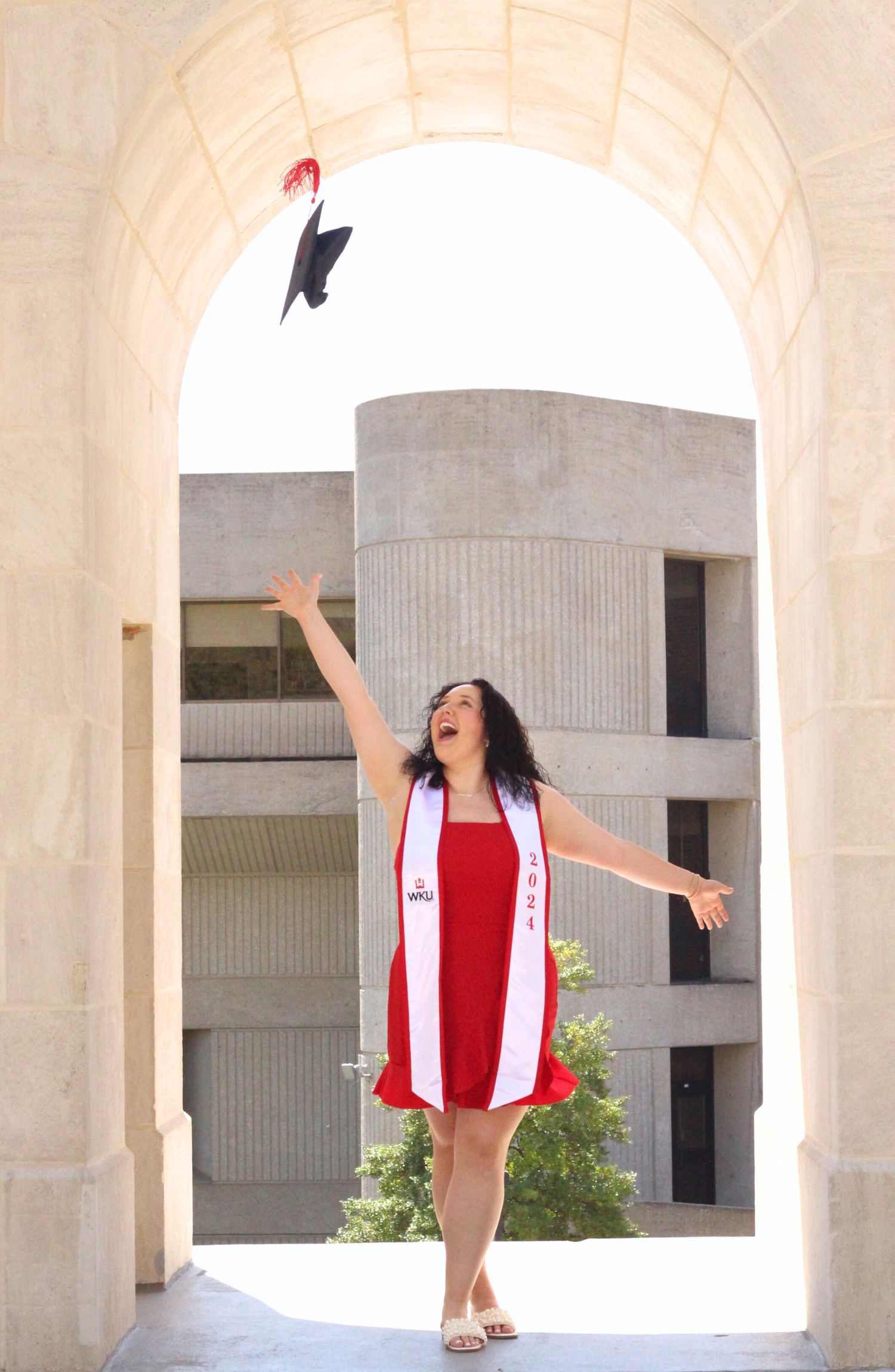 Graduate celebrates enthusiastically under white stone archway.