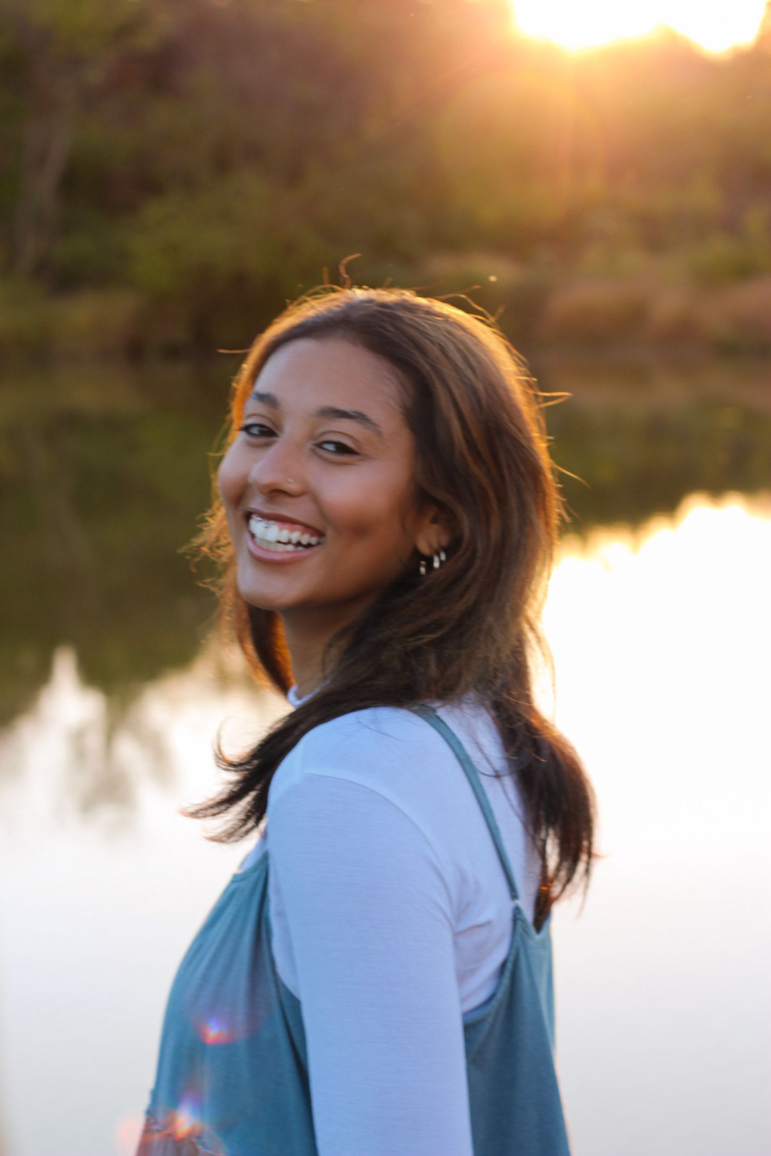 Portrait of a joyful expression at sunset by a lake wearing a white top and blue dress.