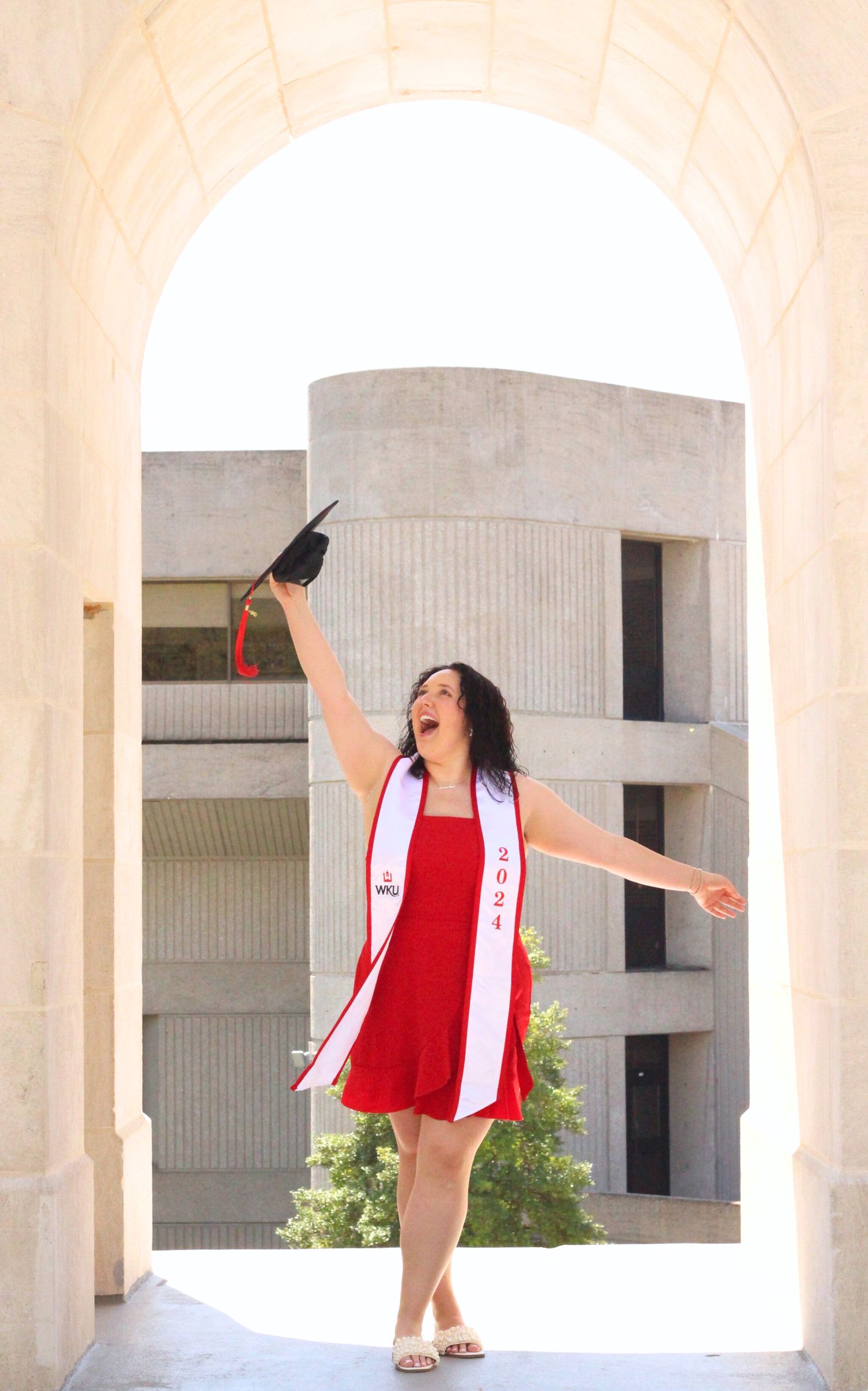 Graduate celebrates with cap toss under arched colonnade.