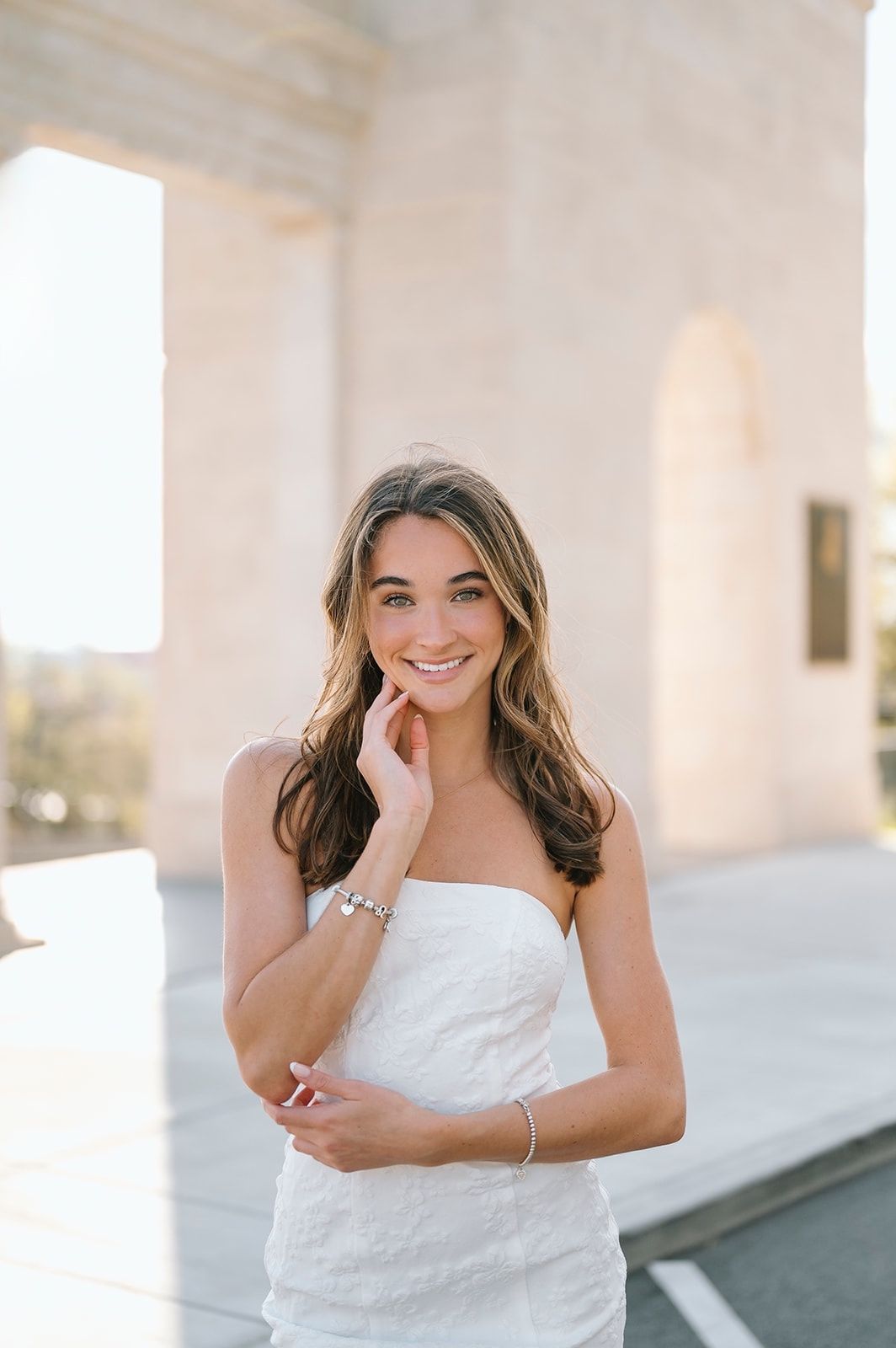 Woman in white dress poses elegantly against white architectural columns.