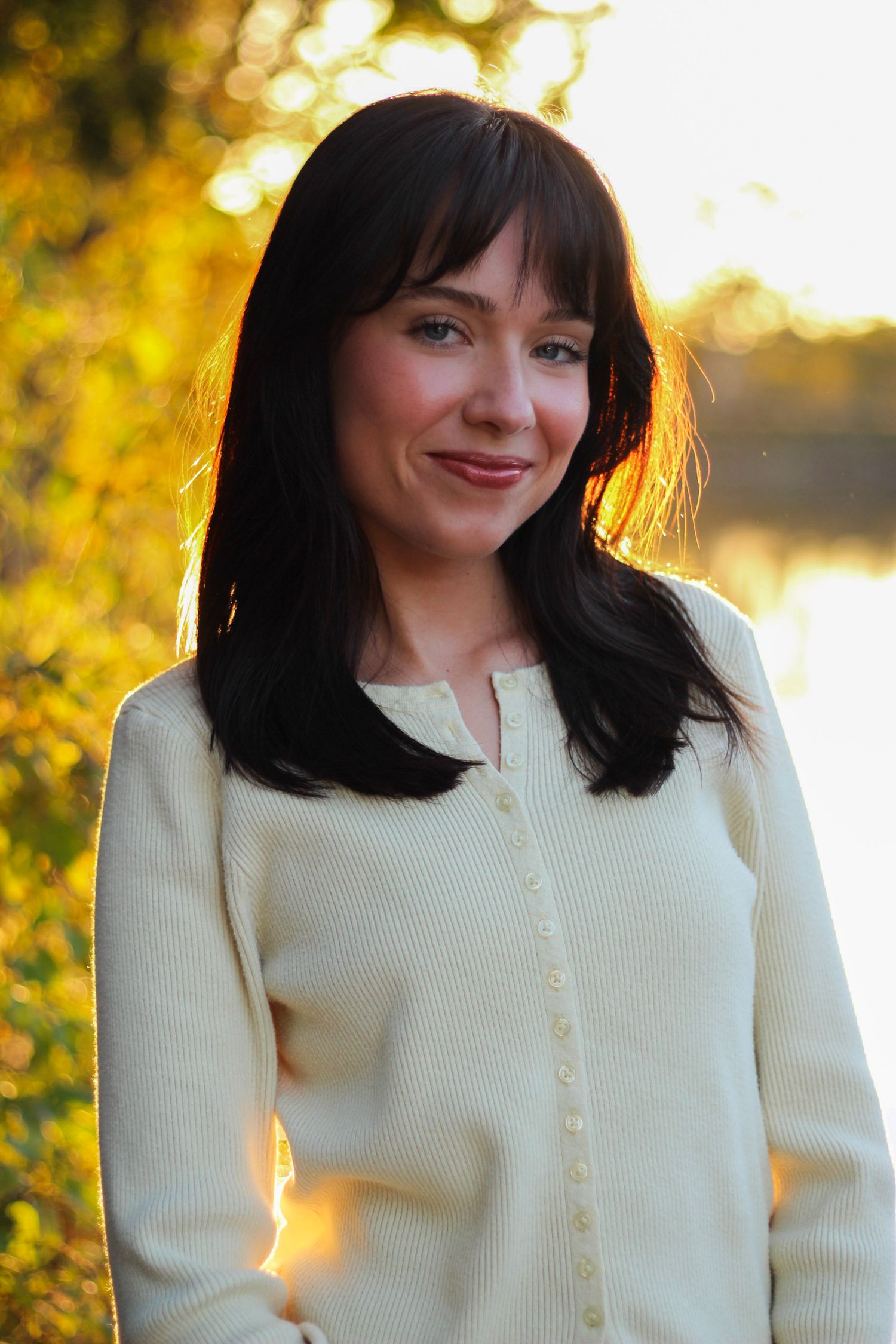 Portrait of someone in a cream cardigan against golden autumn foliage at sunset.