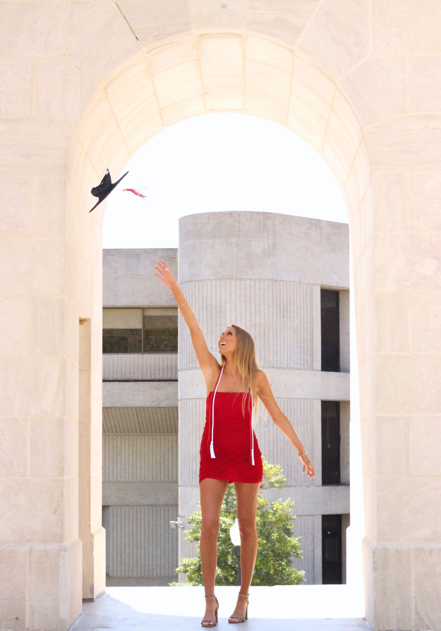 Person in red outfit poses playfully between classical white columns.