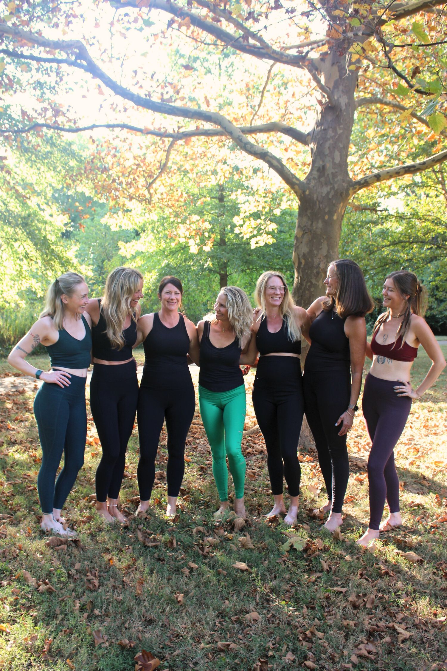Group of yoga practitioners in athletic wear standing together outdoors under autumn trees.
