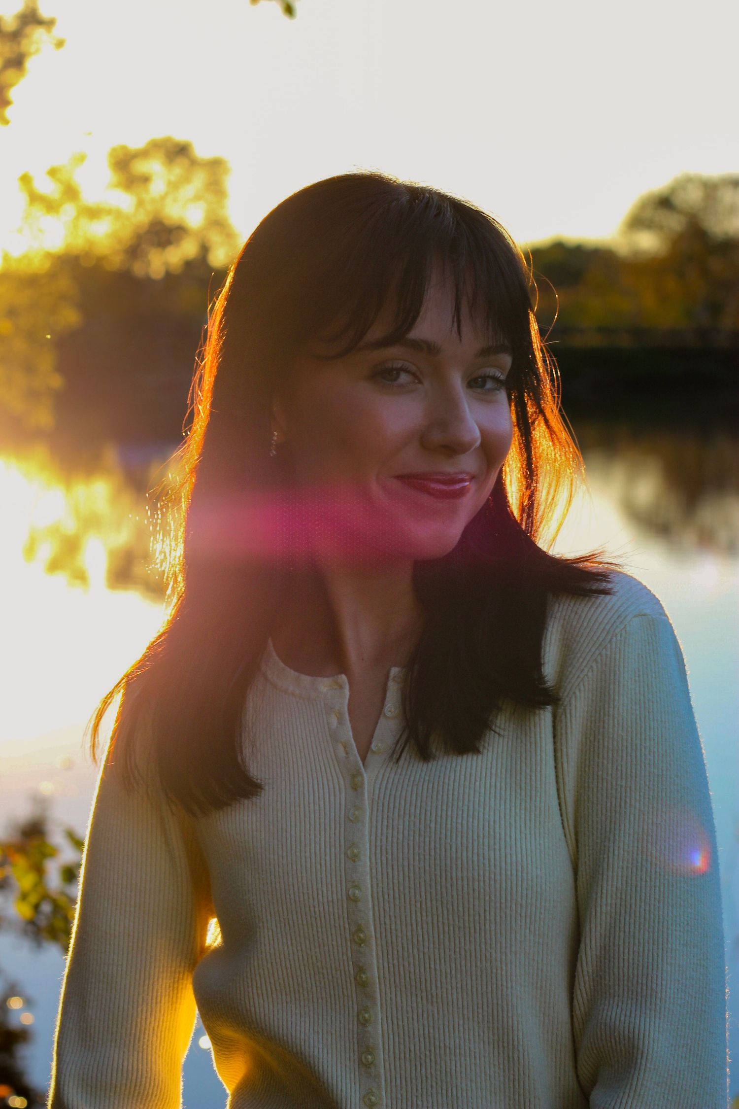 Person wearing a cream sweater poses against golden sunset light reflecting off water.