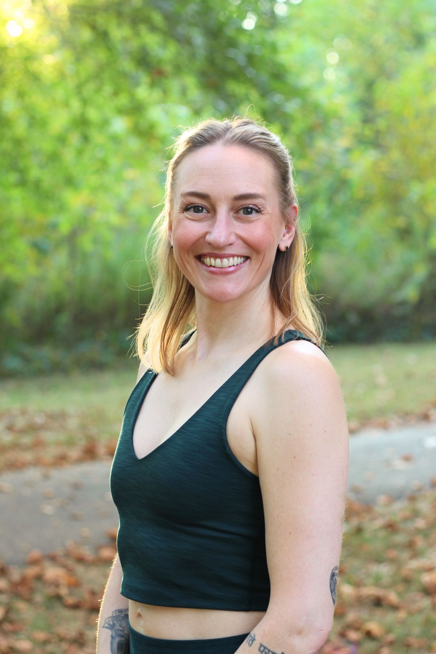 Portrait of yoga instructor in black tank top smiling outdoors.