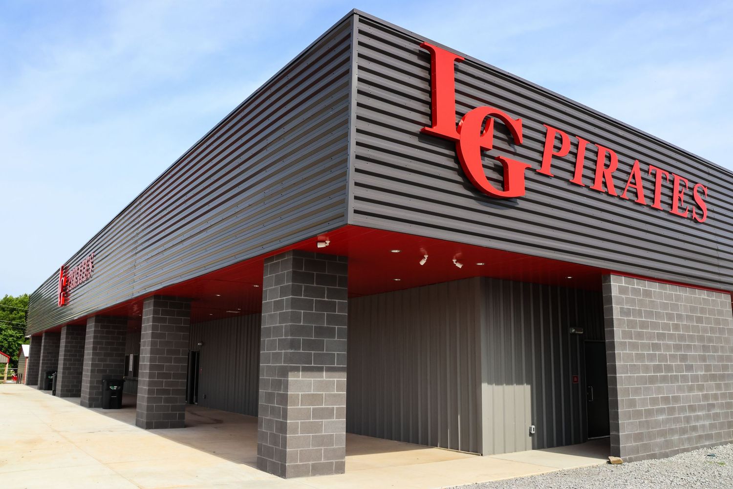 Modern commercial building exterior with gray metal siding and red signage mounted on concrete block walls.