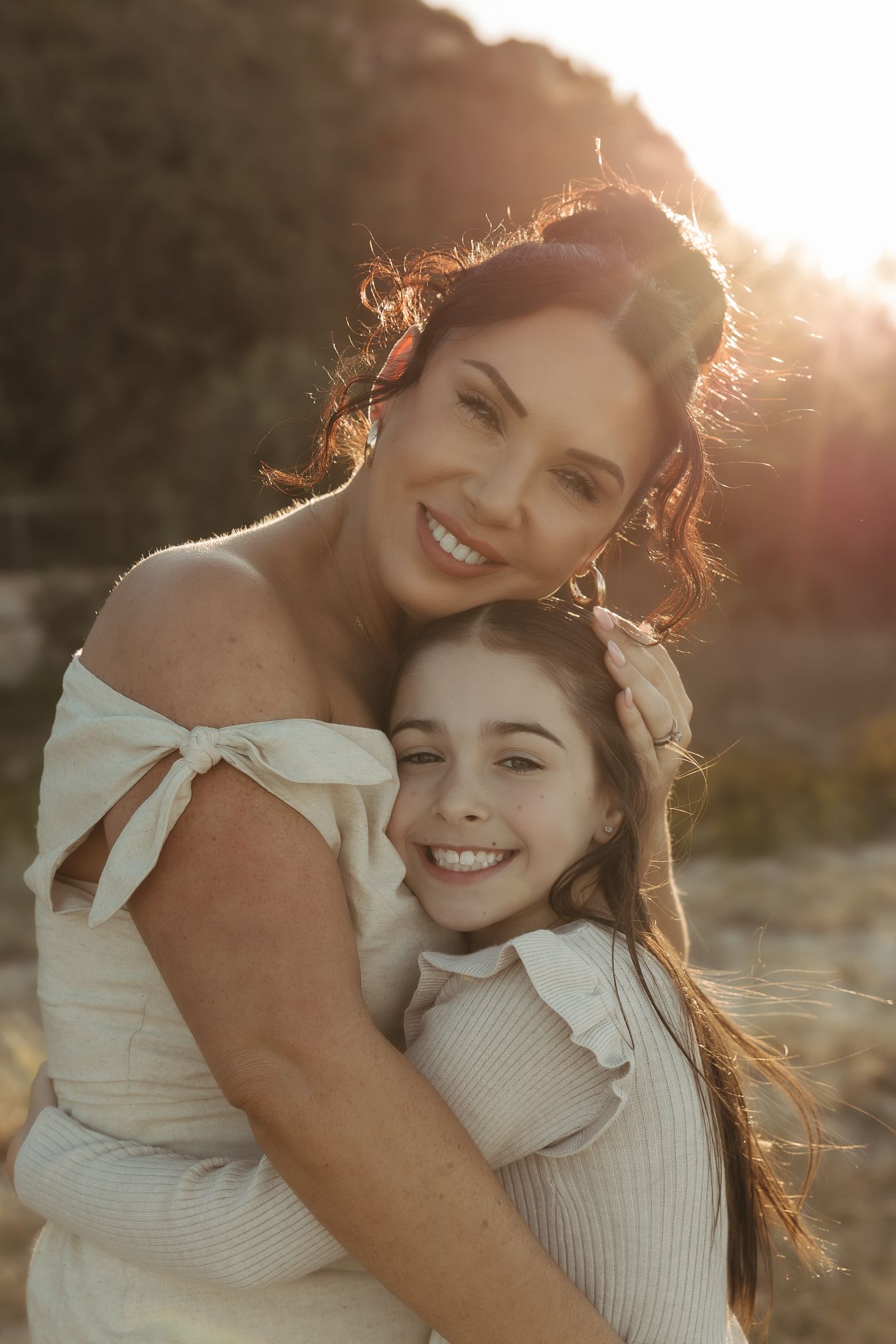 Mother and daughter share joyful embraces during golden hour photoshoot in matching white outfits.