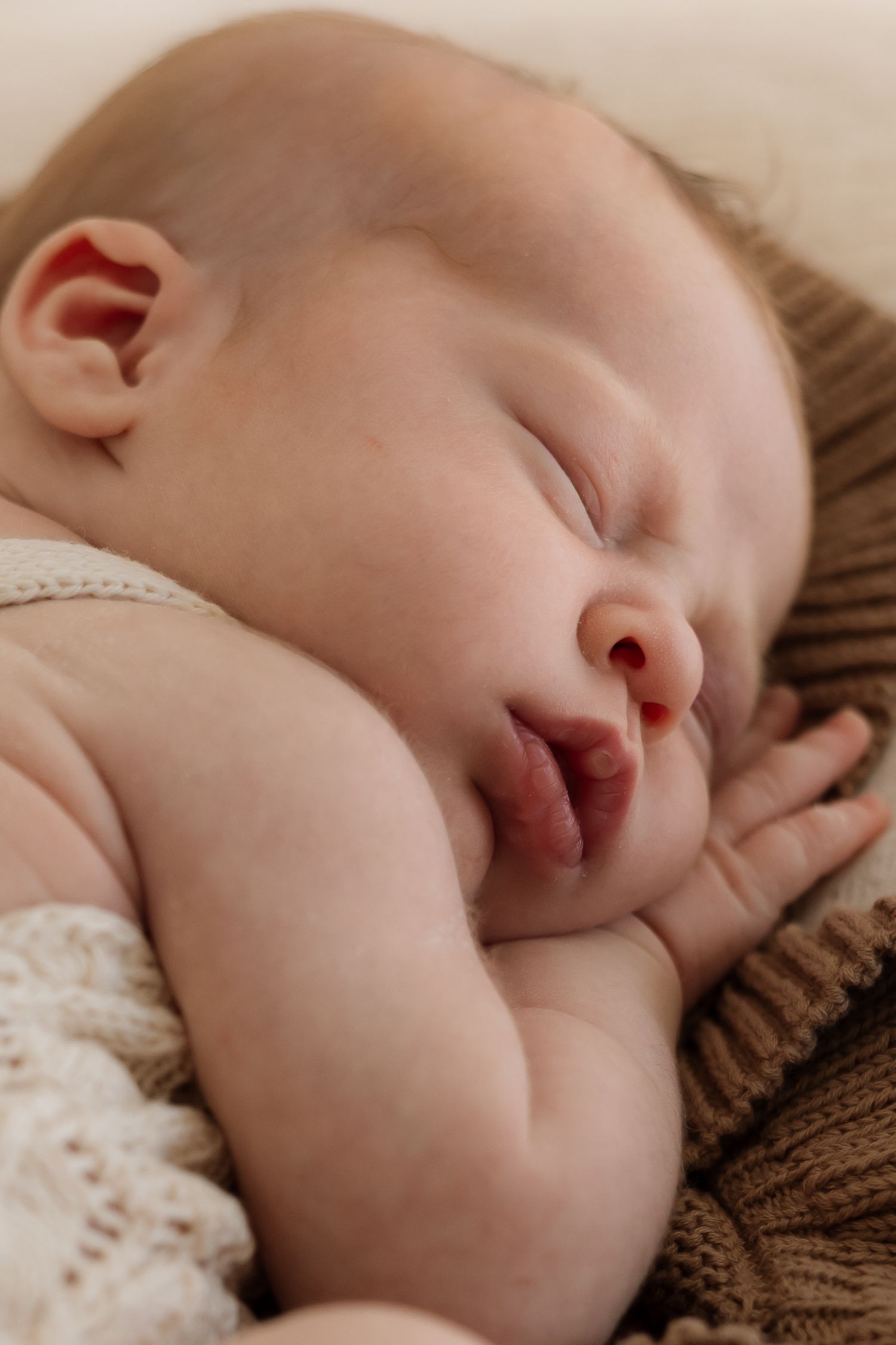 A sleeping baby rests peacefully on brown knit fabric in a series of close-up shots.
