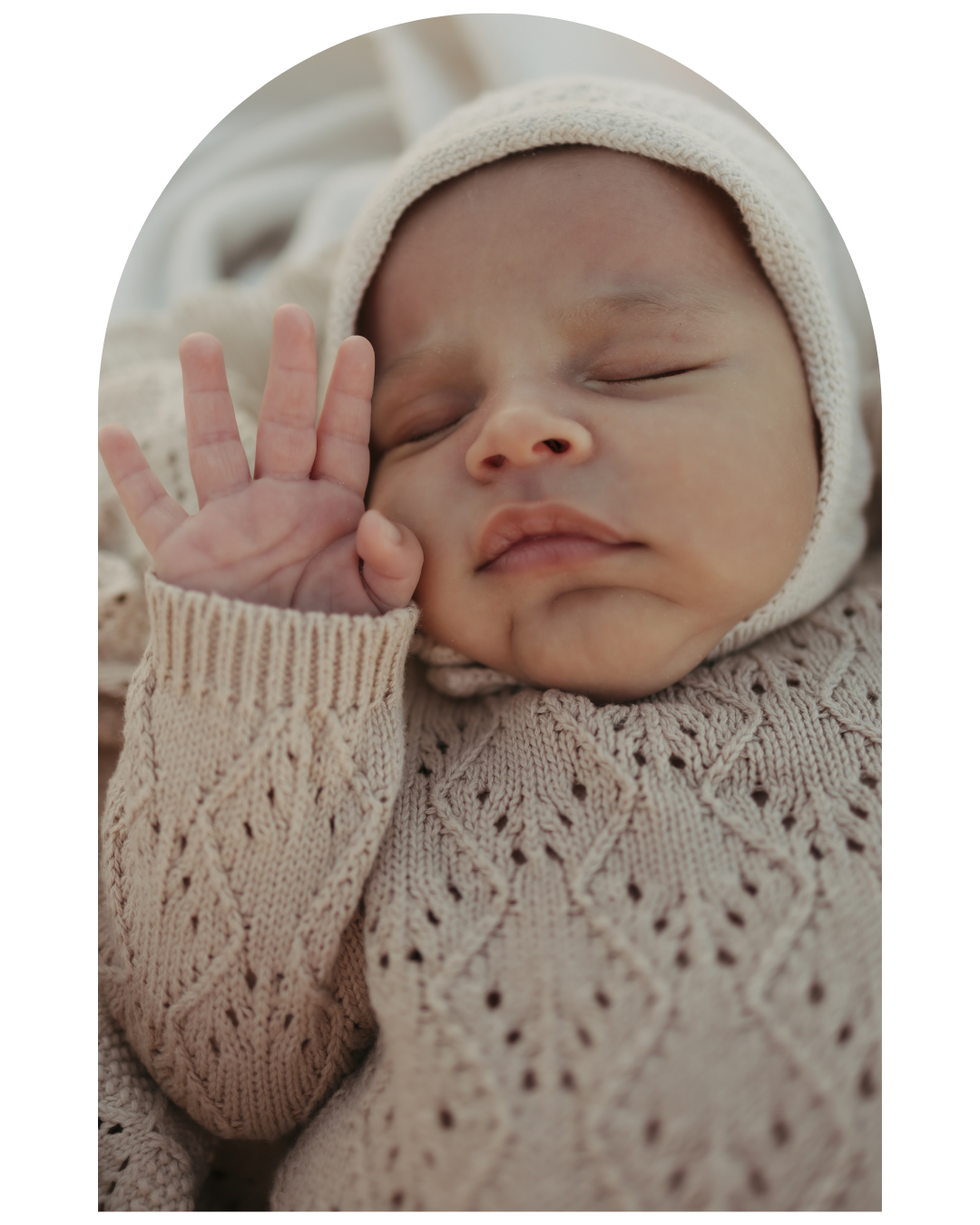 Sleeping newborn baby wearing a knit sweater and hat lying on textured fabric.