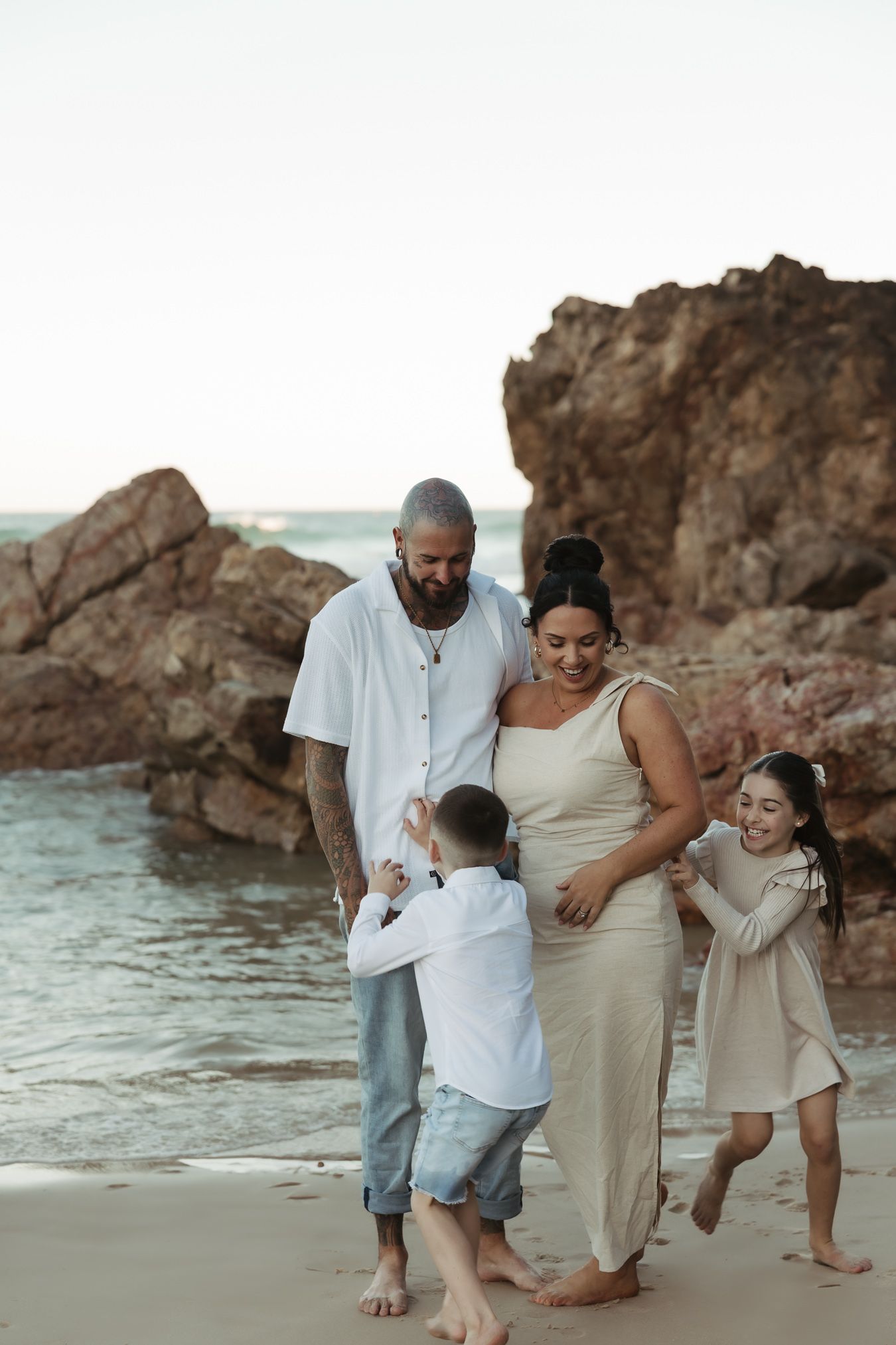 A family shares a joyful moment together on a beach with rocky cliffs during sunset.