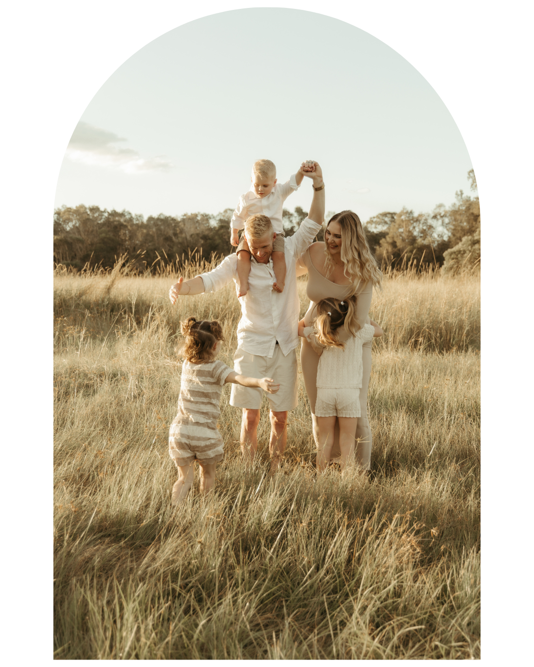 Group wearing white outfits walking together through a sun-lit field of tall grass.