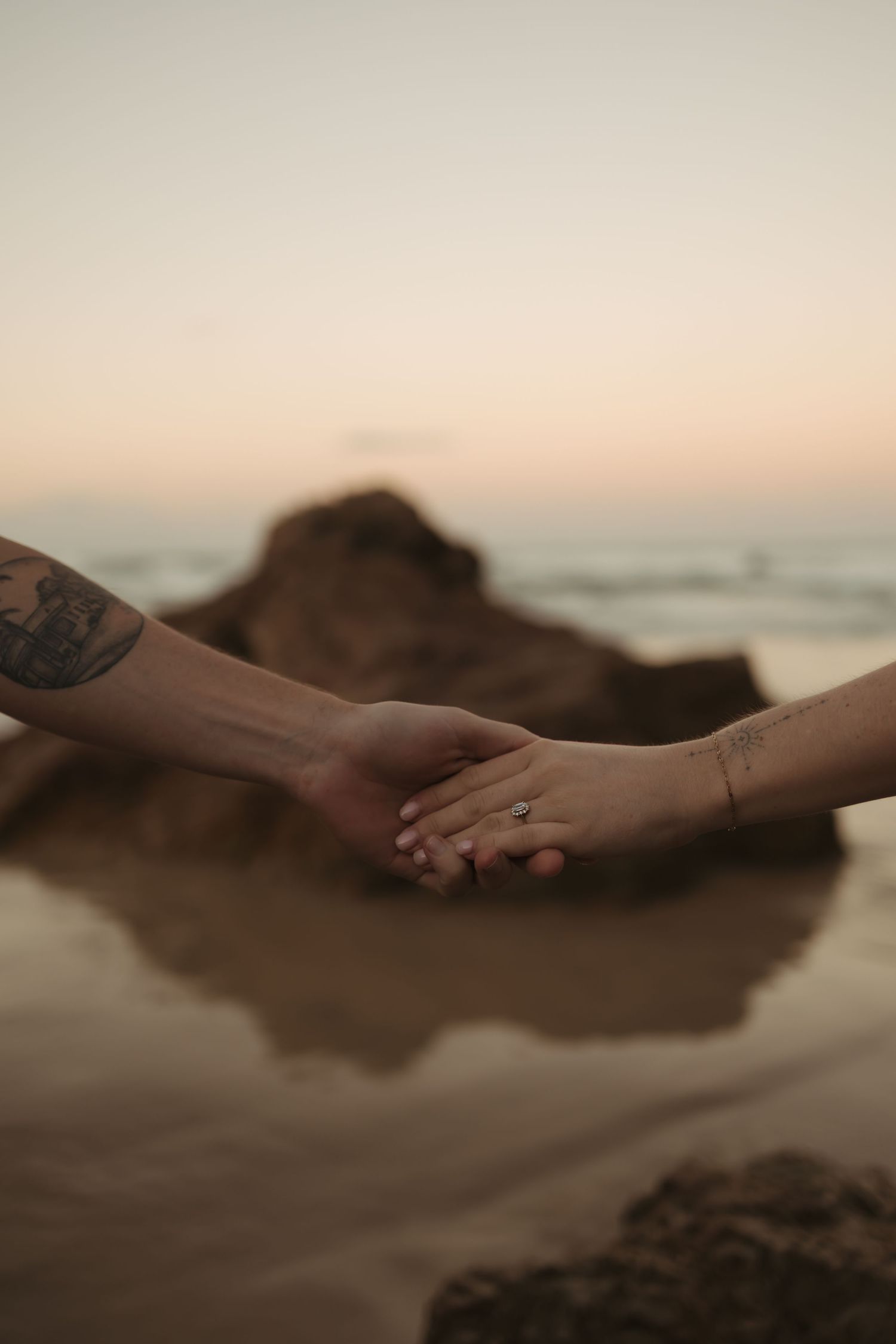 Two hands reaching towards each other on a sandy beach at sunset with soft focus and warm lighting.