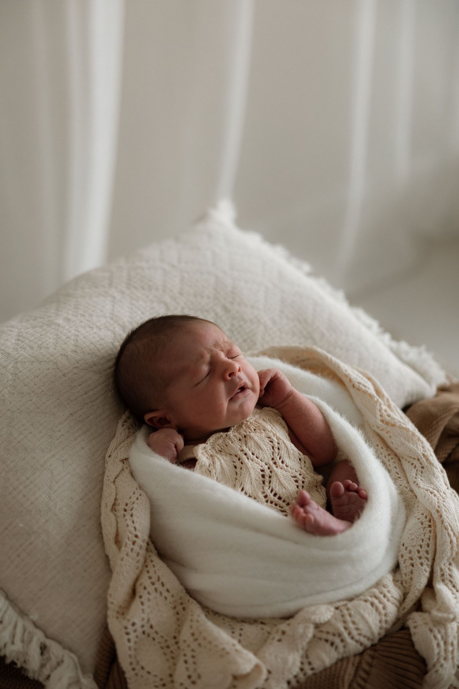 A sleeping newborn wrapped in soft white blankets lies on a textured knit surface in a series of connected images.