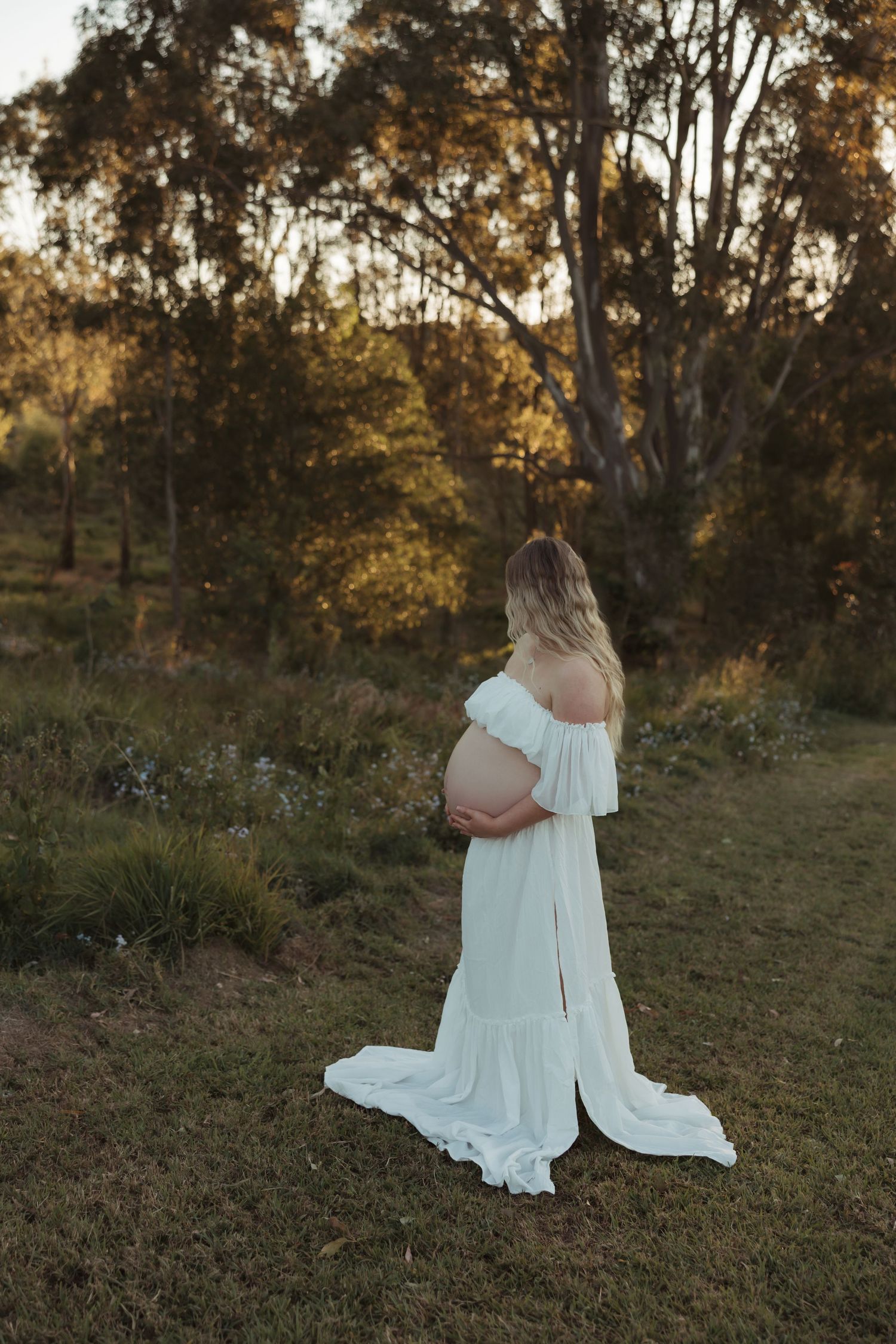 Ethereal maternity portraits in flowing white dress against golden sunset.