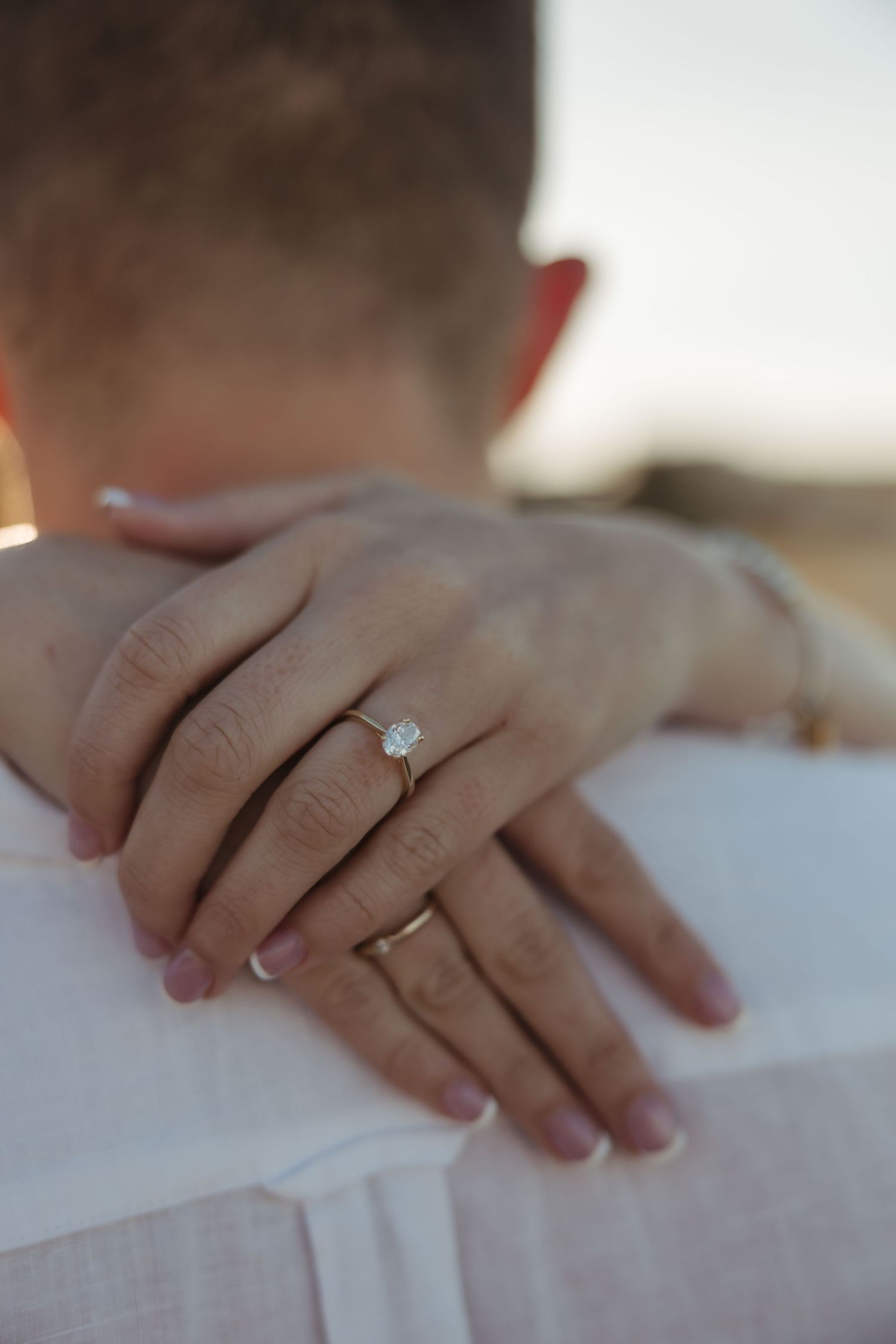 Close-up of hands showing engagement ring with diamond solitaire during romantic sunset moment.