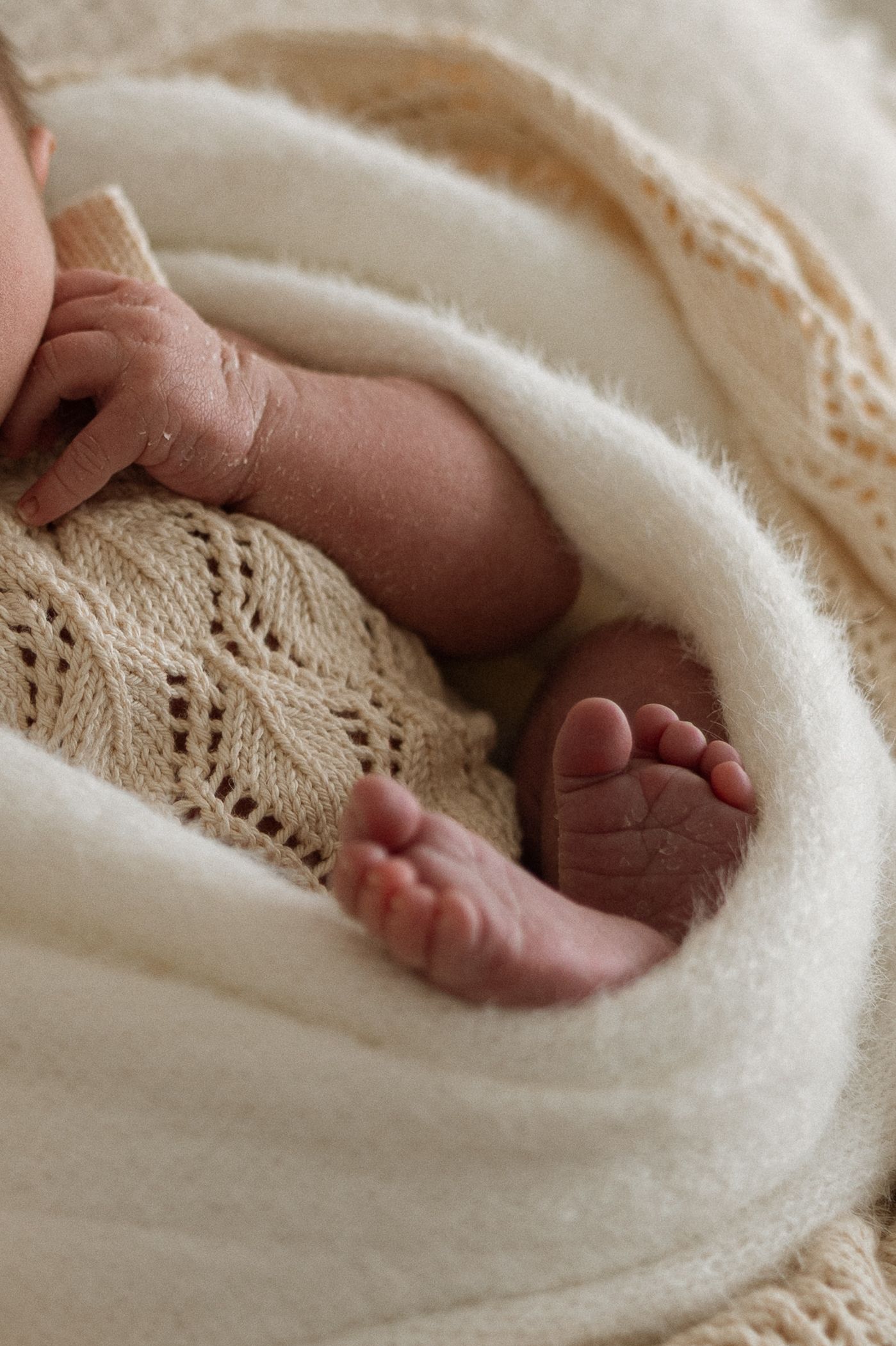 Close-up view of tiny baby feet resting on delicate lace and soft white blanket material.