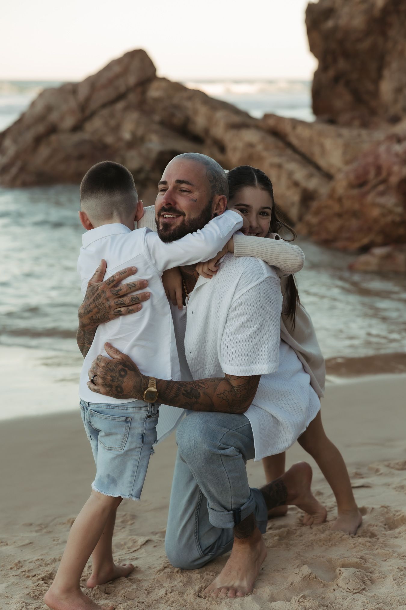 A heartwarming embrace shared between family members on a rocky beach at sunset with ocean waves in the background.