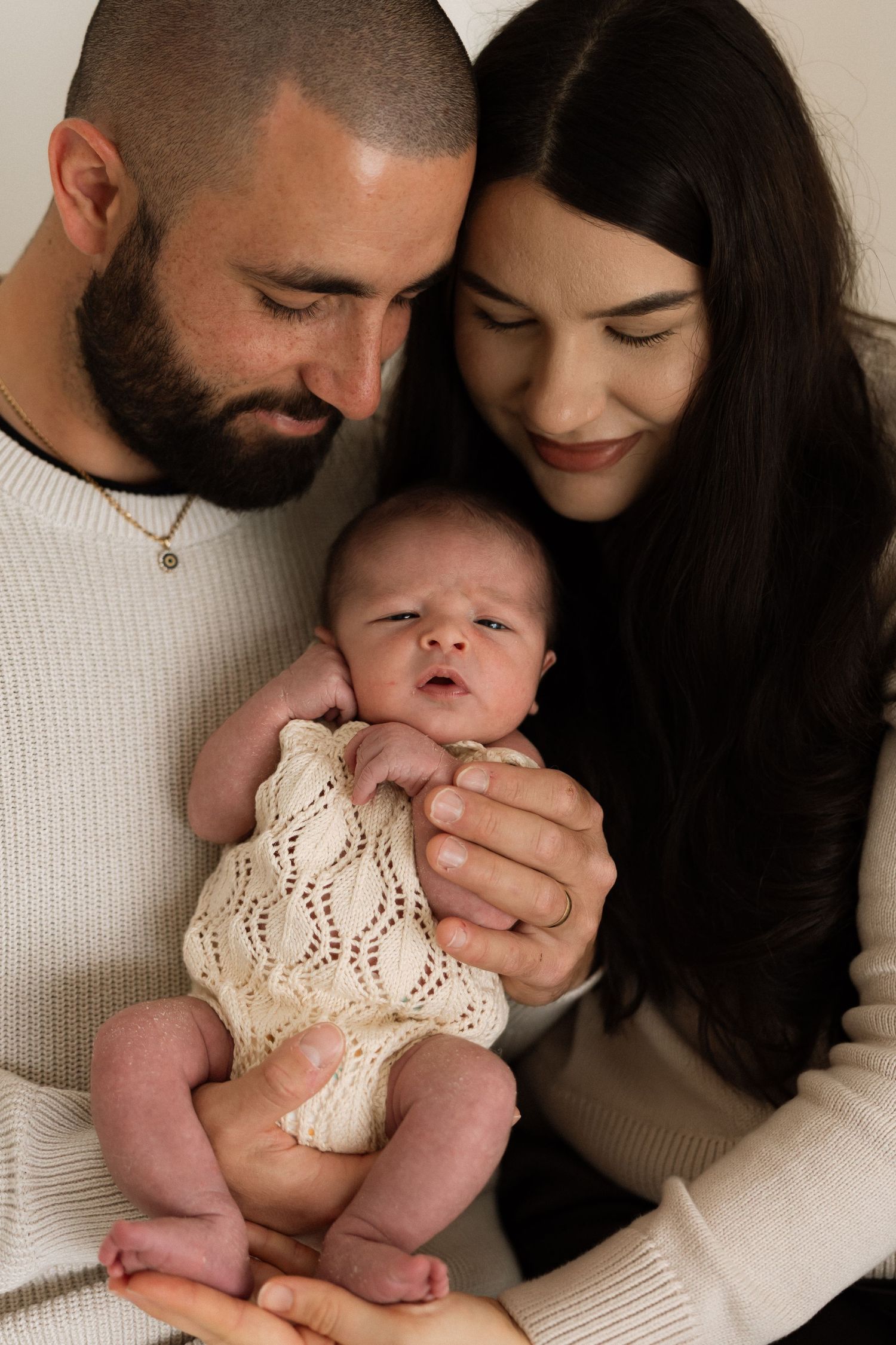 A couple in white and black clothing cuddles with their newborn baby in a series of tender intimate moments.