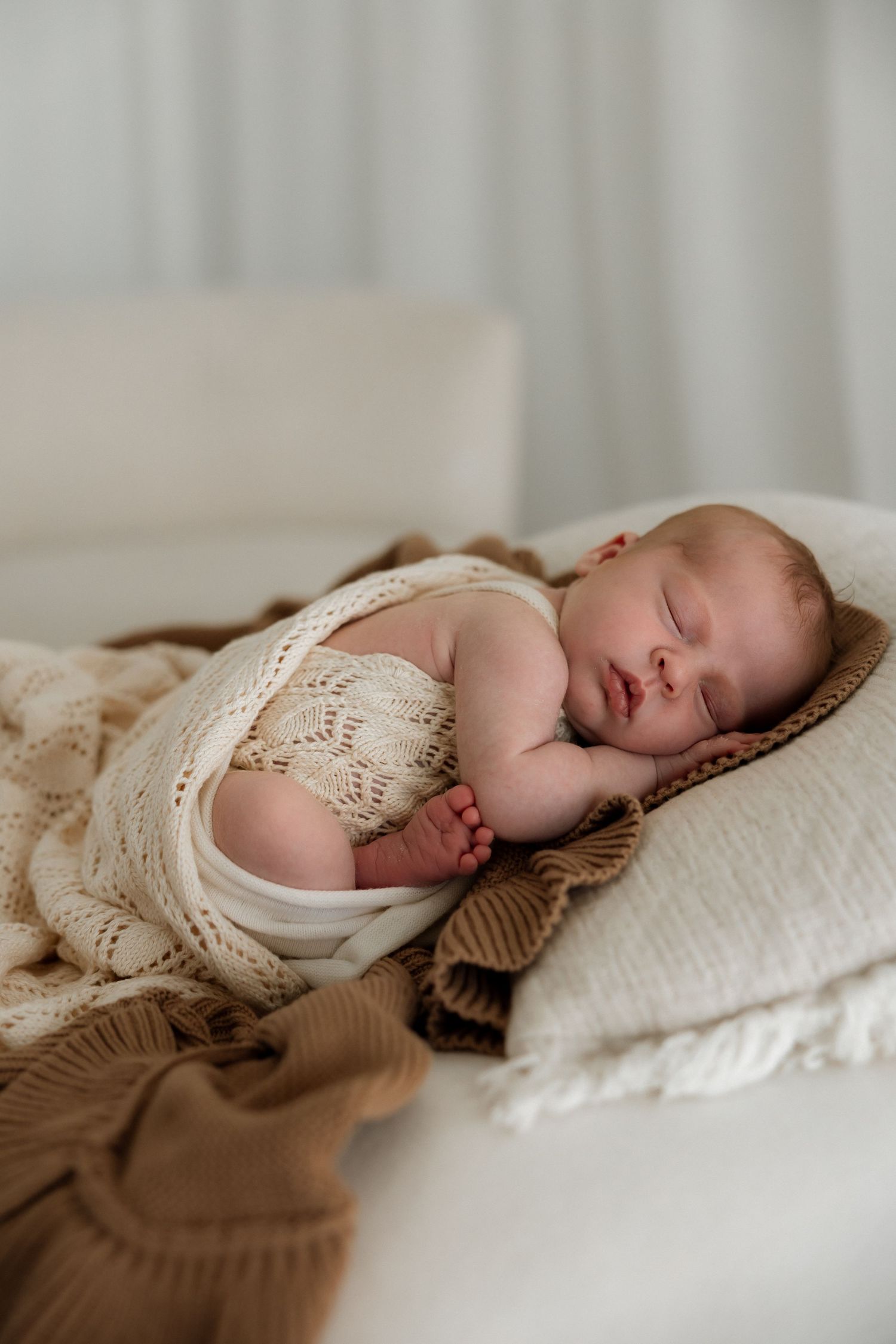 Sleeping baby in white knit romper lying peacefully on cozy blankets in soft natural lighting.