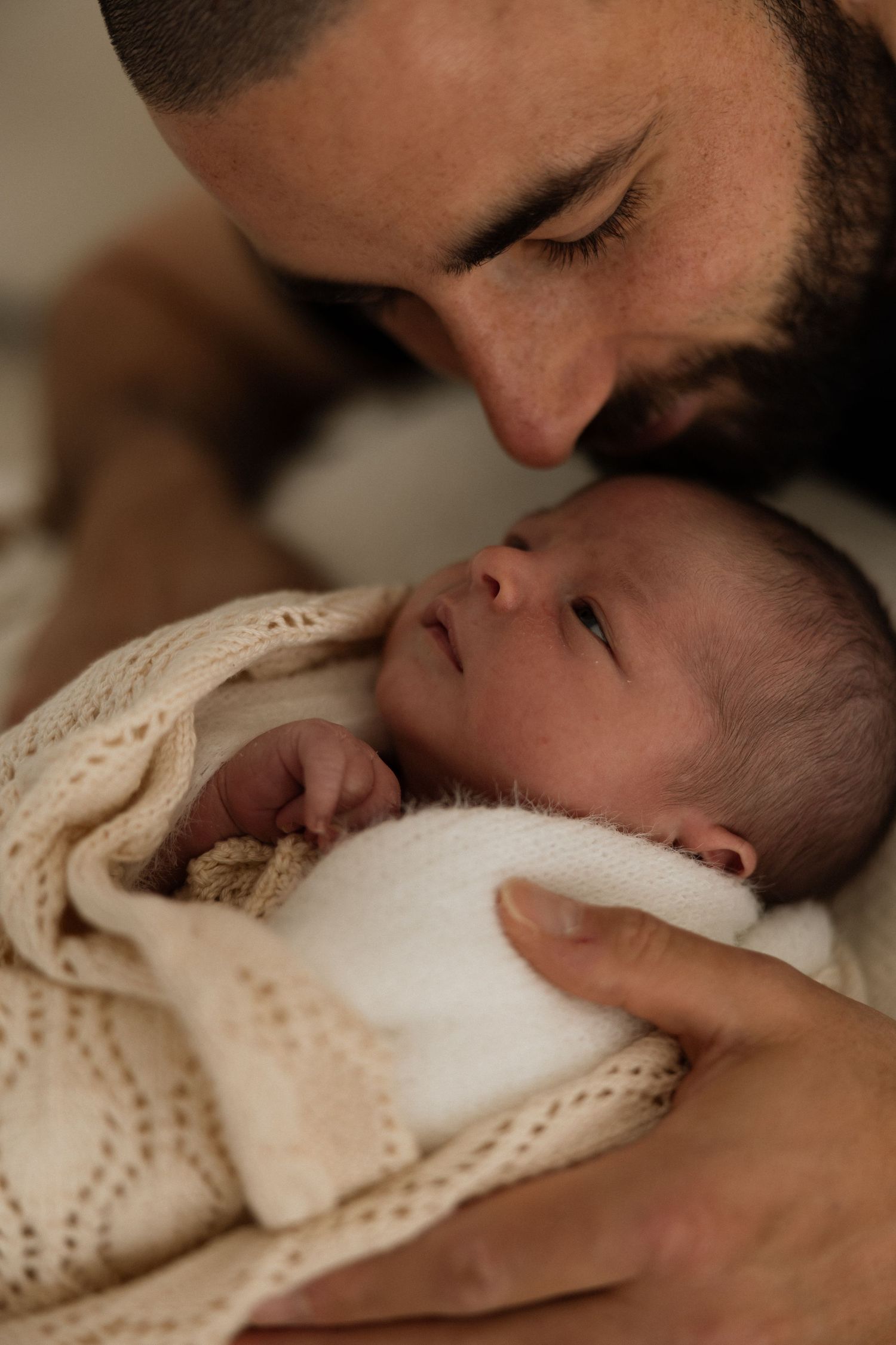 A tender moment captured in a series of photos showing a parent gently kissing their newborn baby wrapped in a knit blanket.