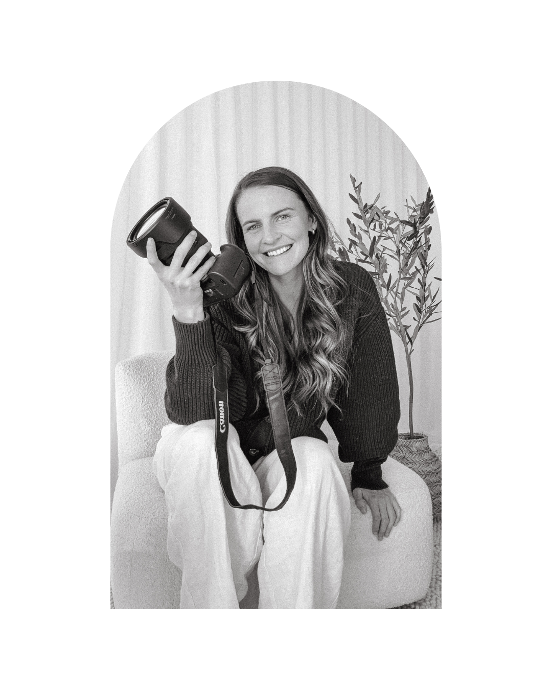 Monochrome portrait of photographer displaying camera equipment in casual indoor setting.