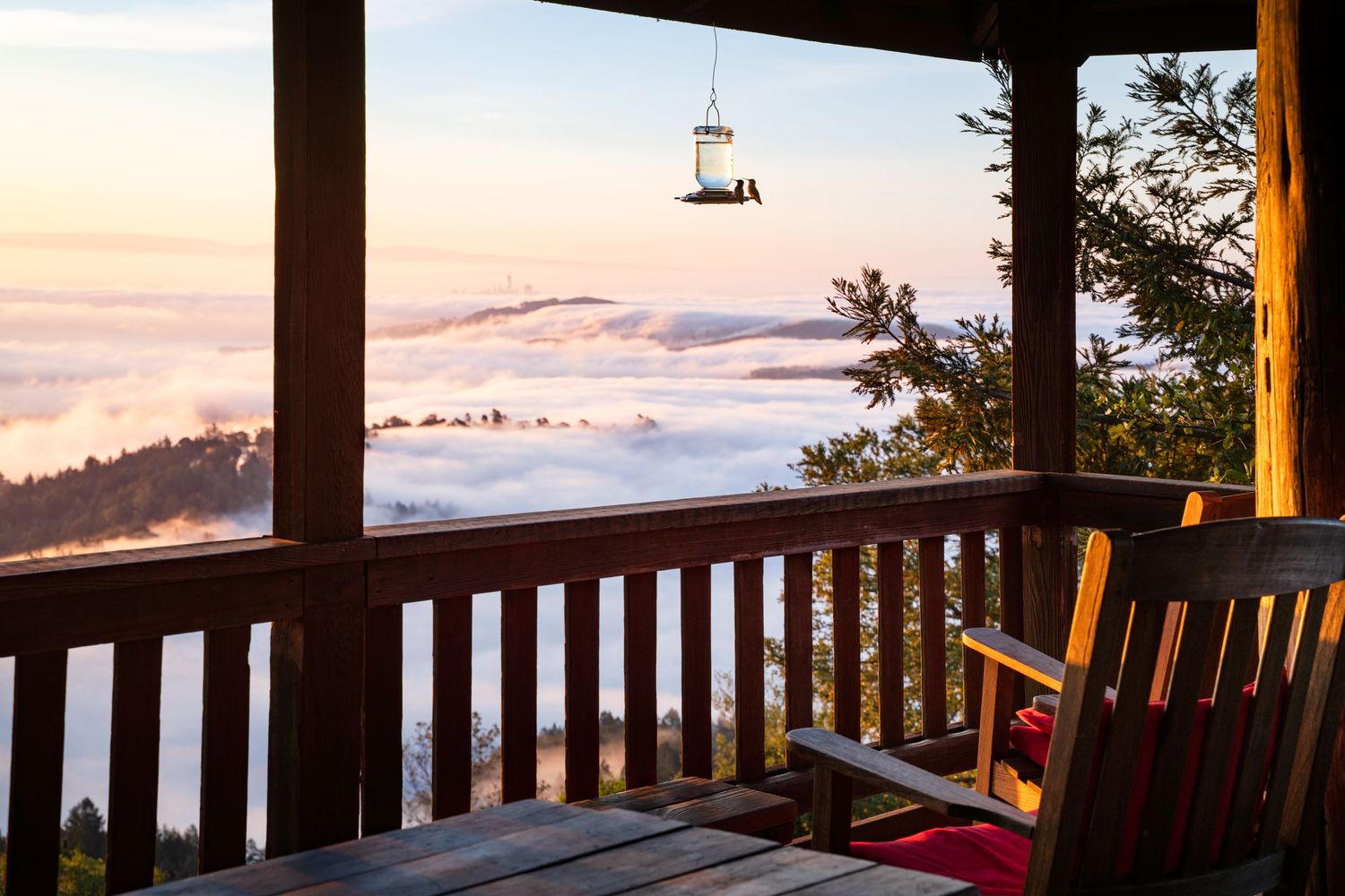 A wooden deck railing overlooking a scenic mountain landscape at sunset with wooden chairs for viewing.