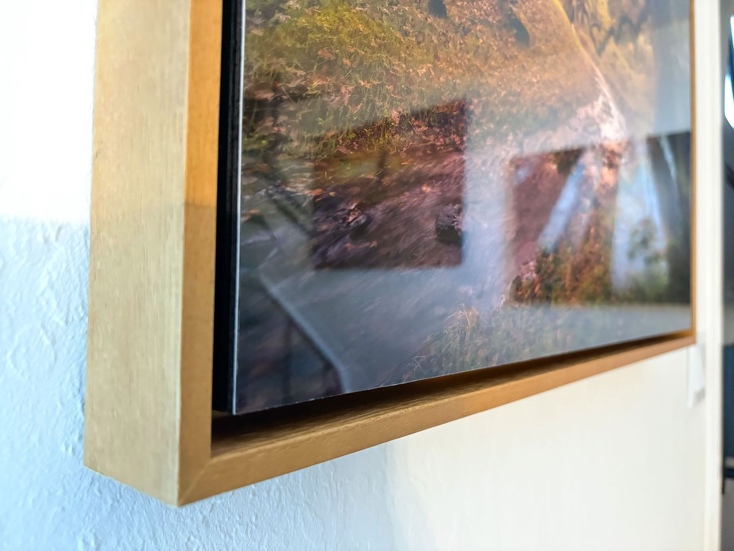 Close-up view of a framed photograph corner showing a wooden frame edge against a light blue wall.