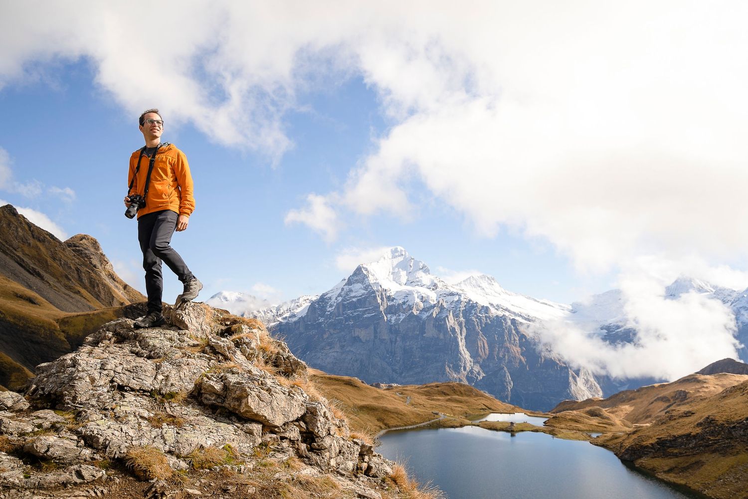 Hiker standing on rocky outcrop overlooking alpine mountains and lake in Switzerland. Owner of Escaype Print Lab.