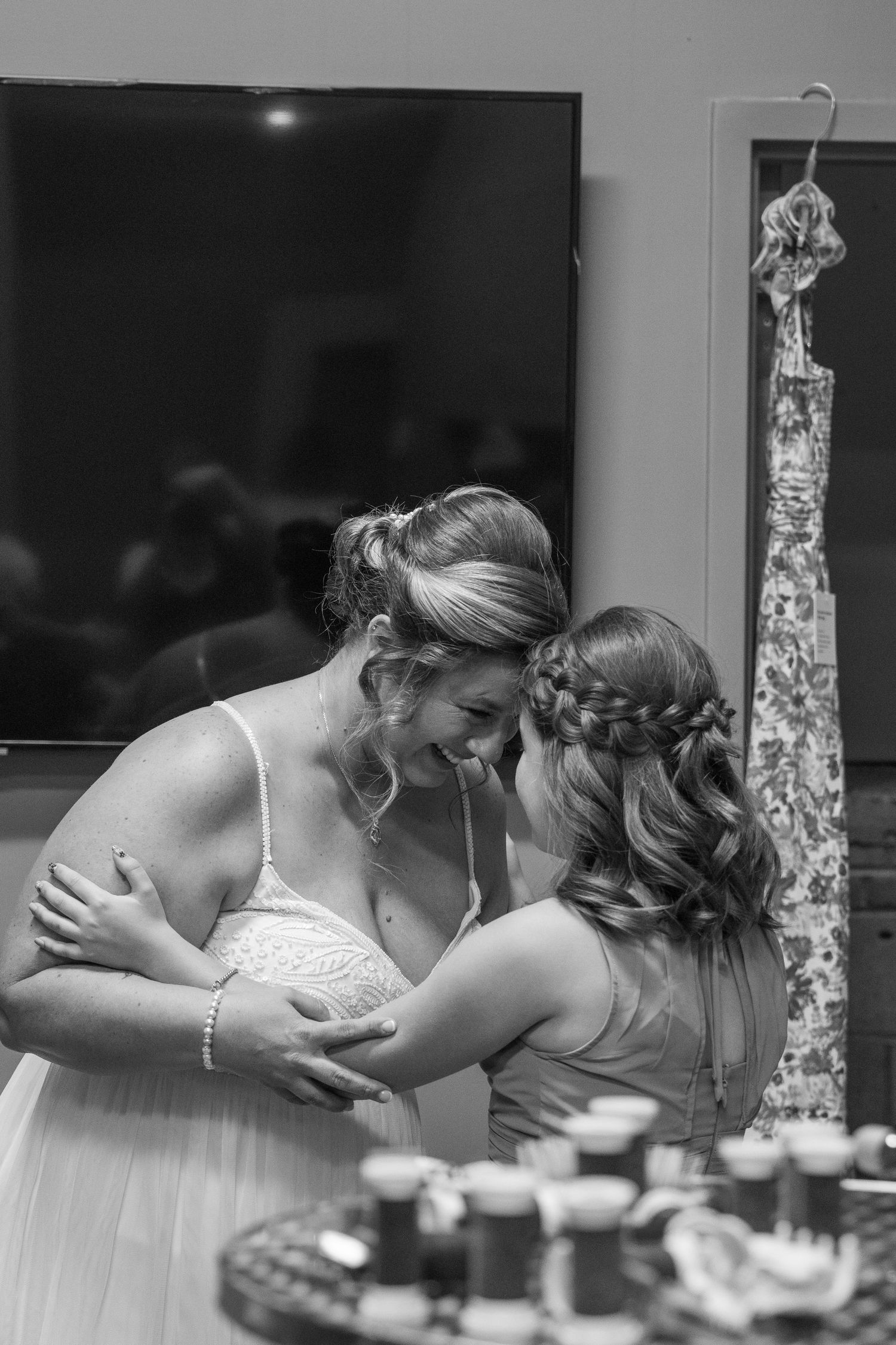 Black and white photo of two women in formal dresses sharing a tender embrace at a wedding celebration.