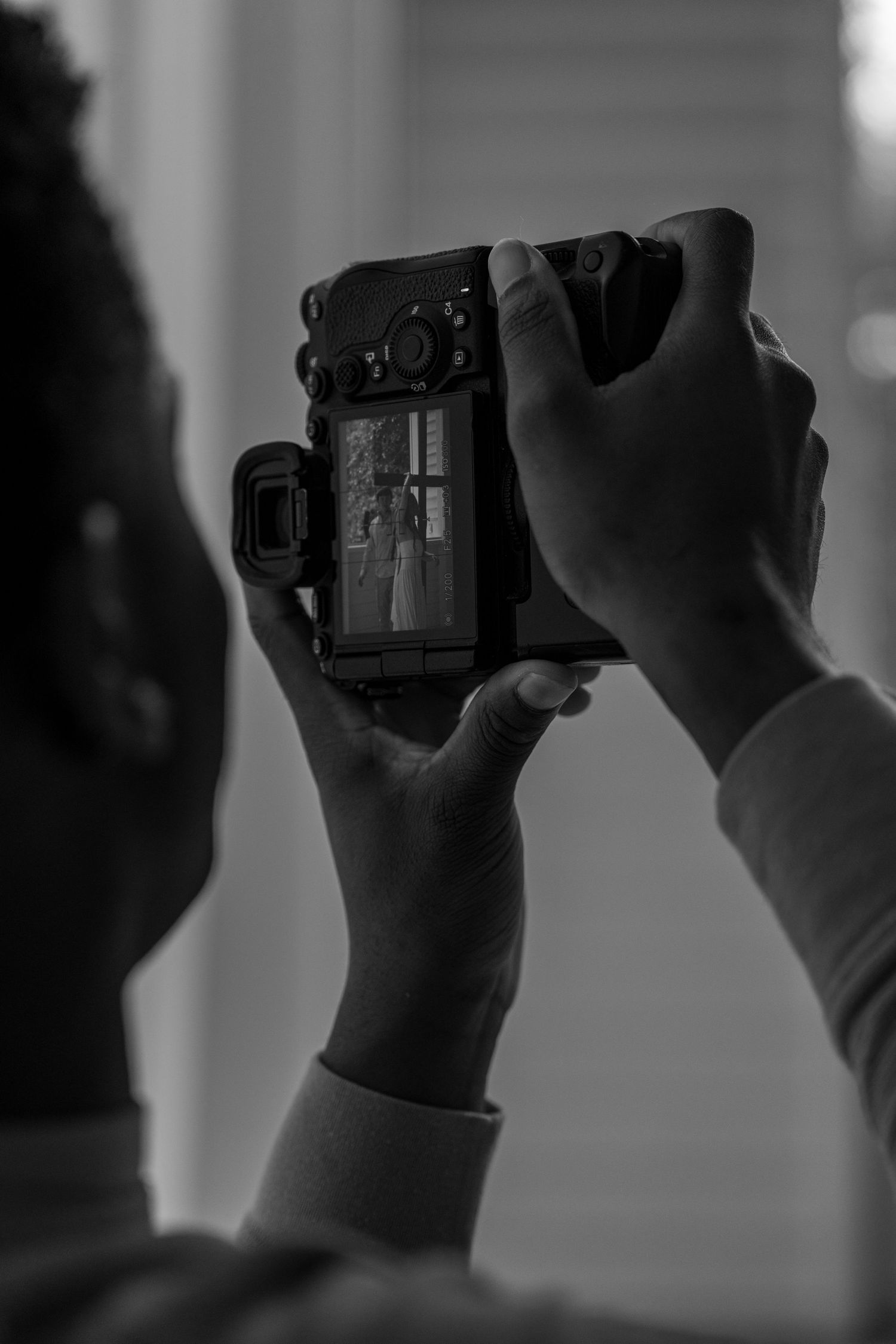 Black and white photo of photographer reviewing wedding couple image on camera LCD screen.