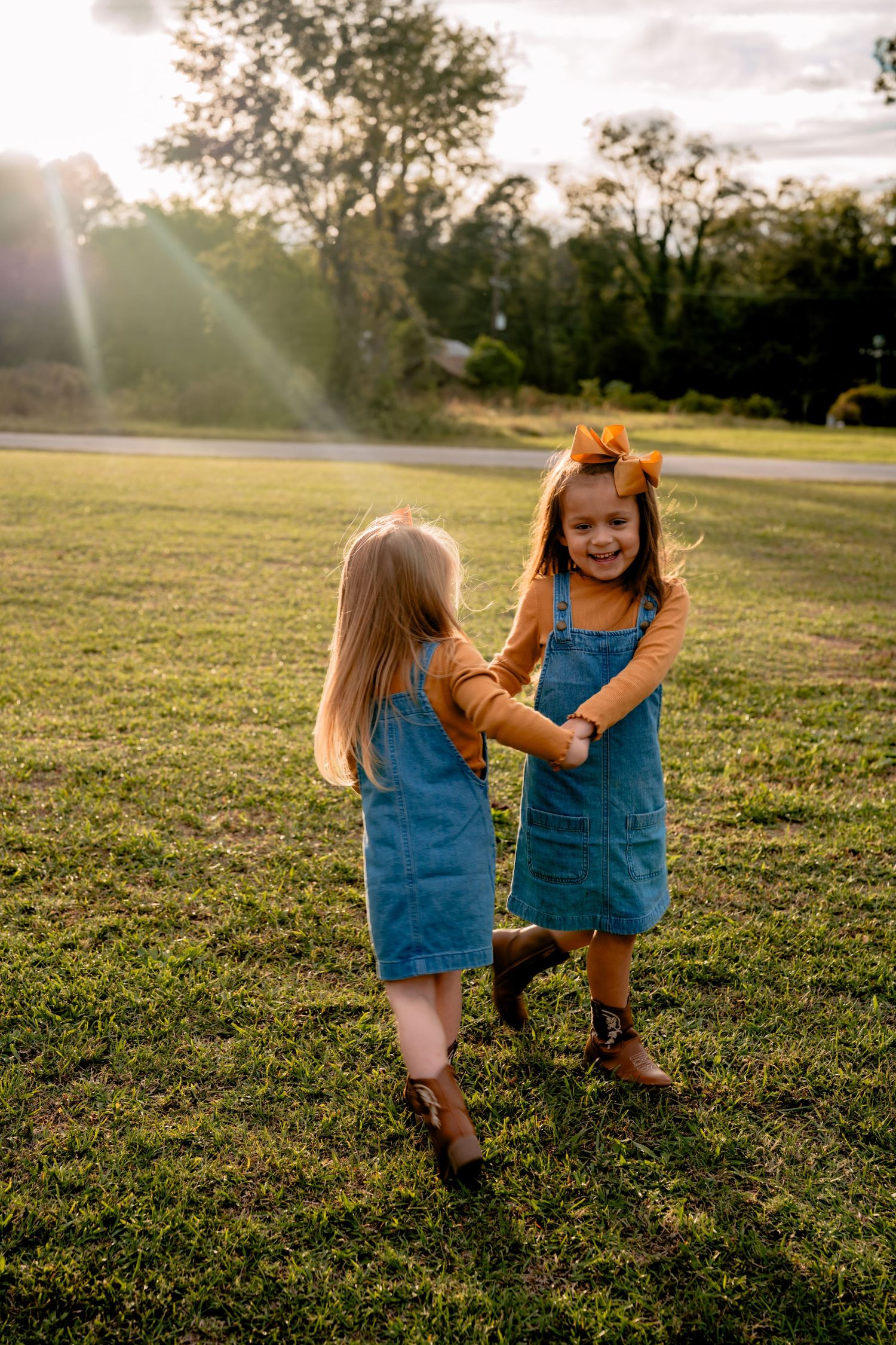 Two children in matching denim outfits running and playing in a sunlit field.