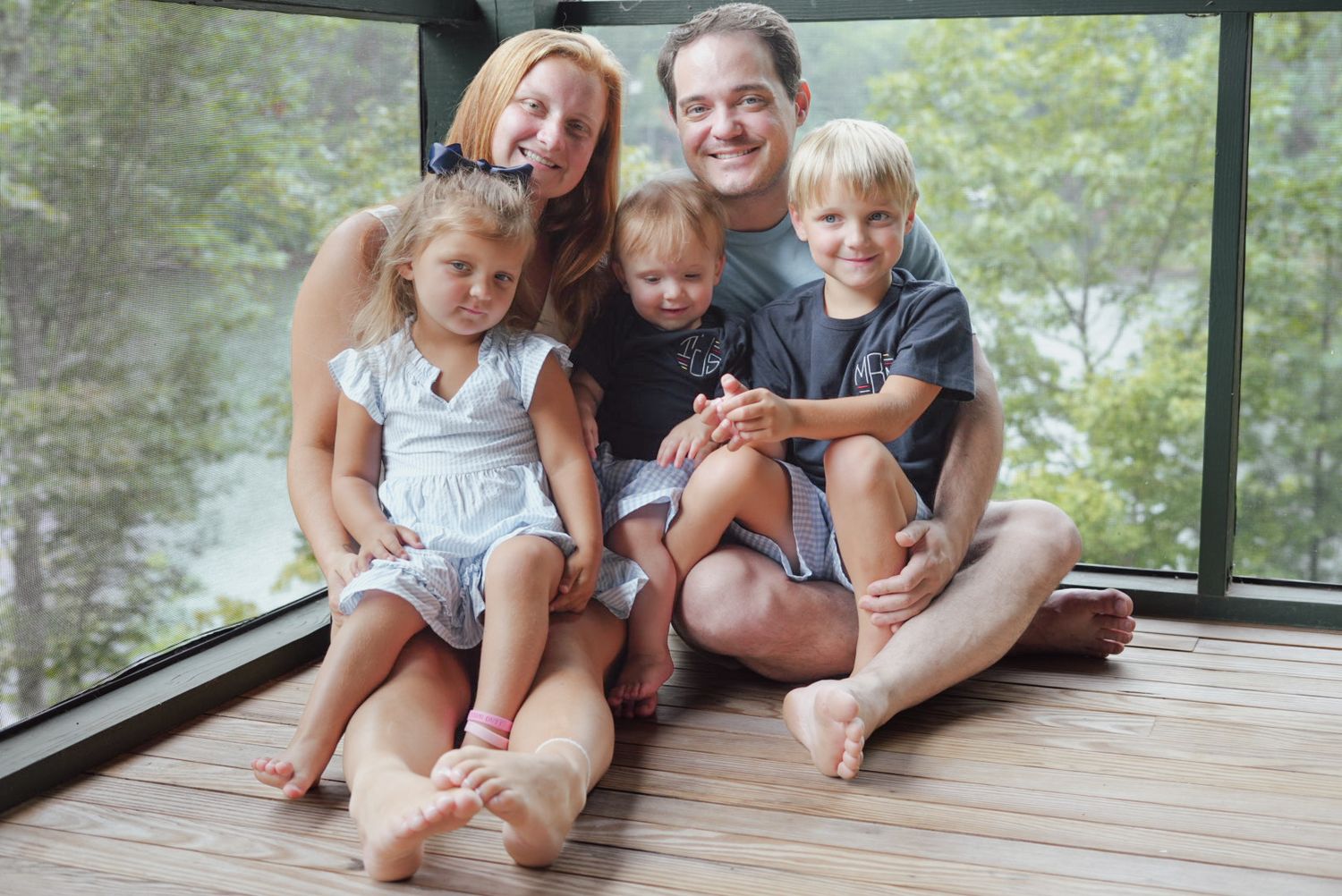 Family sitting together on wooden deck overlooking water on sunny day.