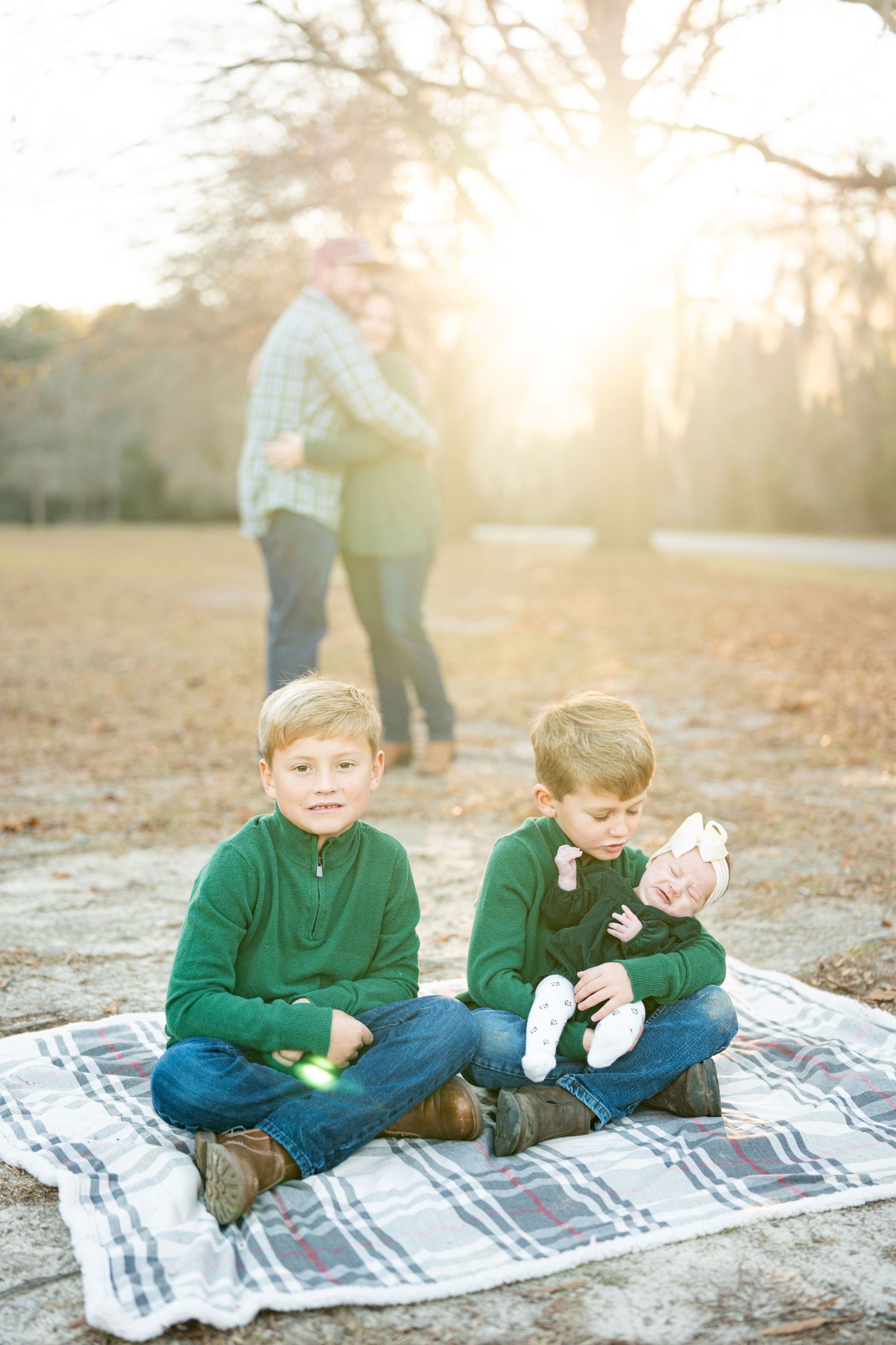 Two children sit together on a plaid blanket outdoors during golden hour sunset.