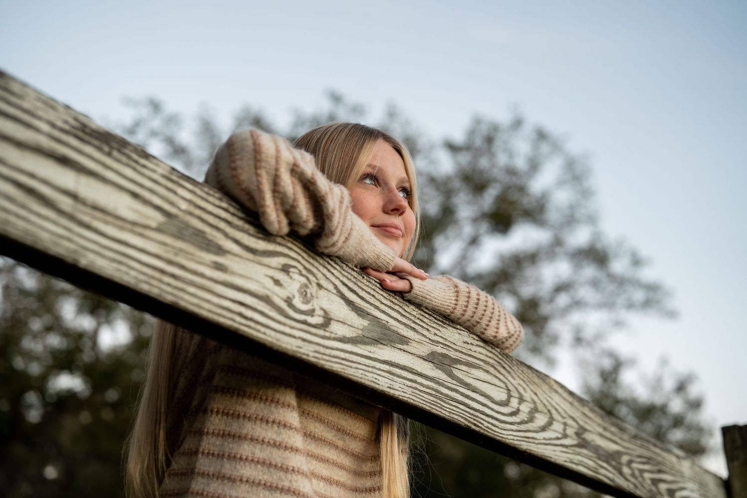 Child in striped sweater playing on wooden fence outdoors.