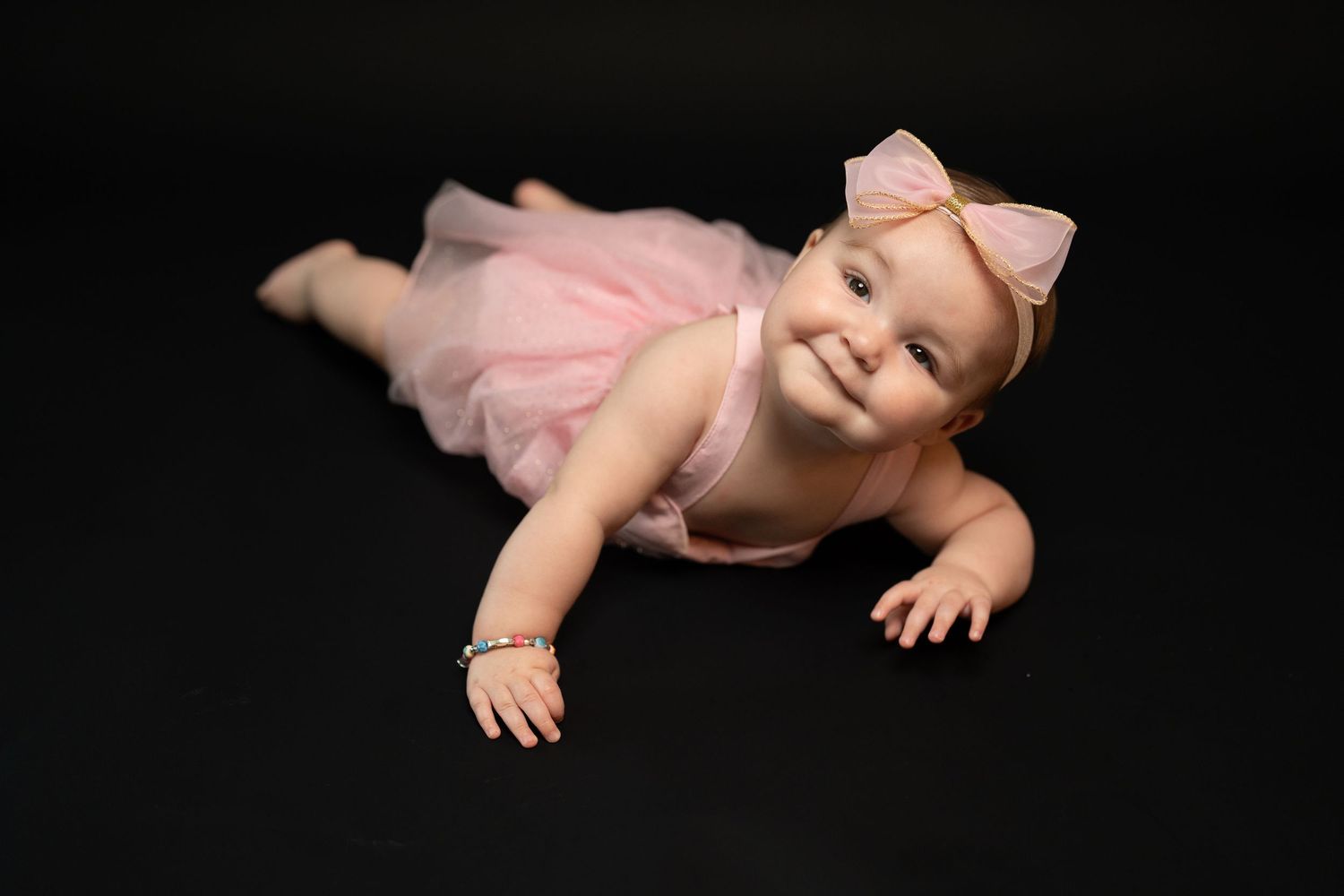 Baby wearing pink outfit lying on black background in artistic poses.