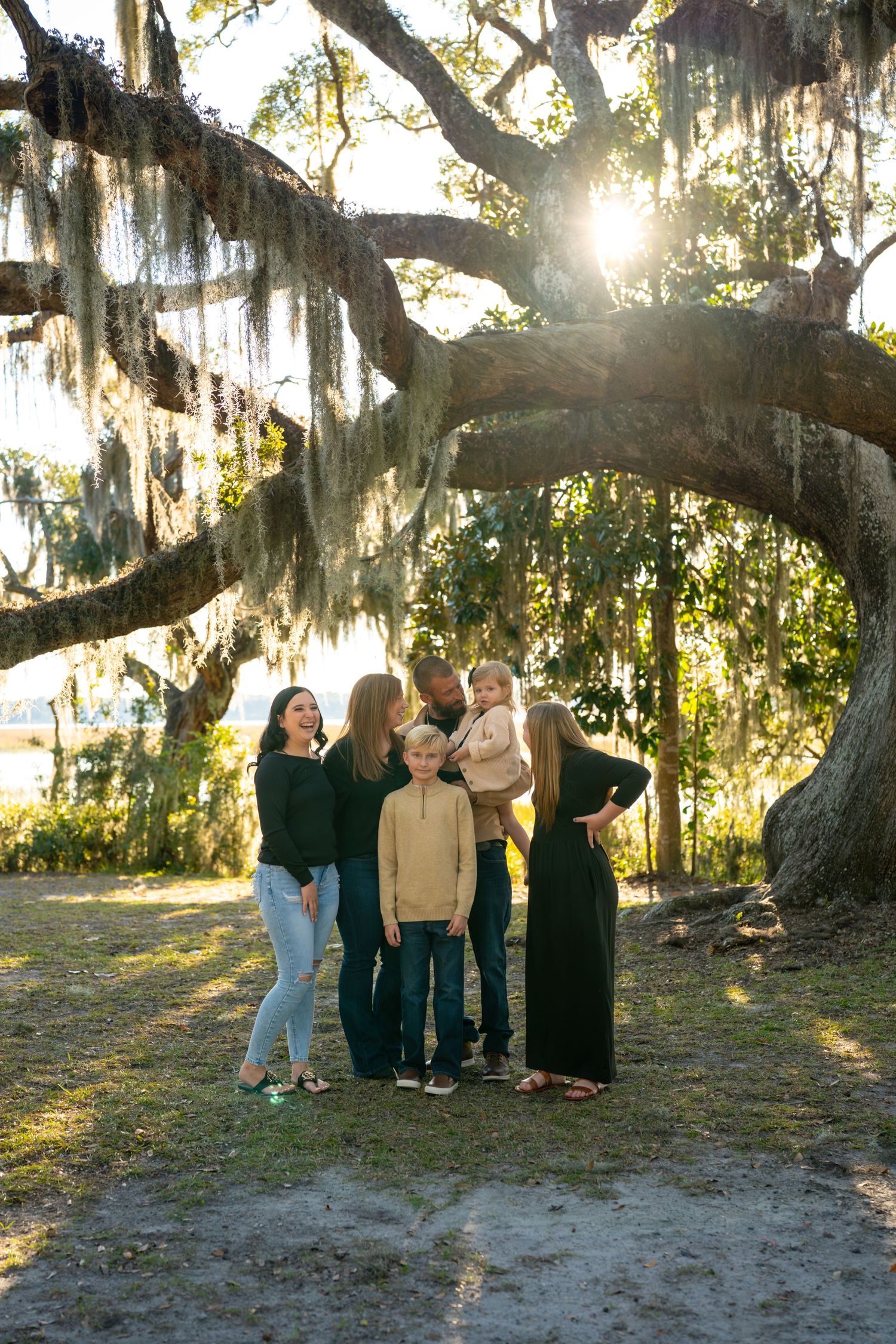 Group gathering beneath a majestic oak tree draped with Spanish moss at sunset.