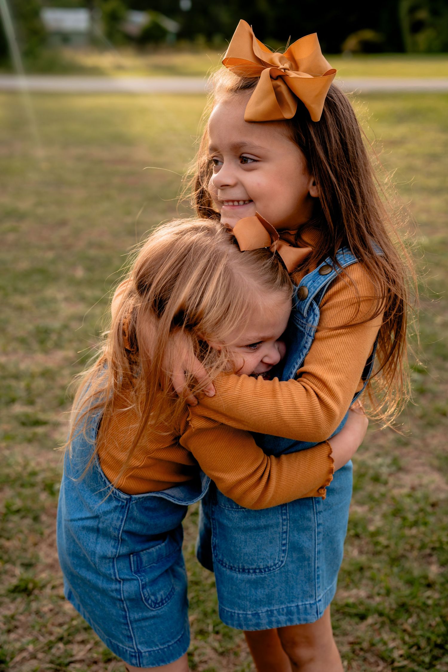 Two children in denim and orange sharing playful hugs outdoors.