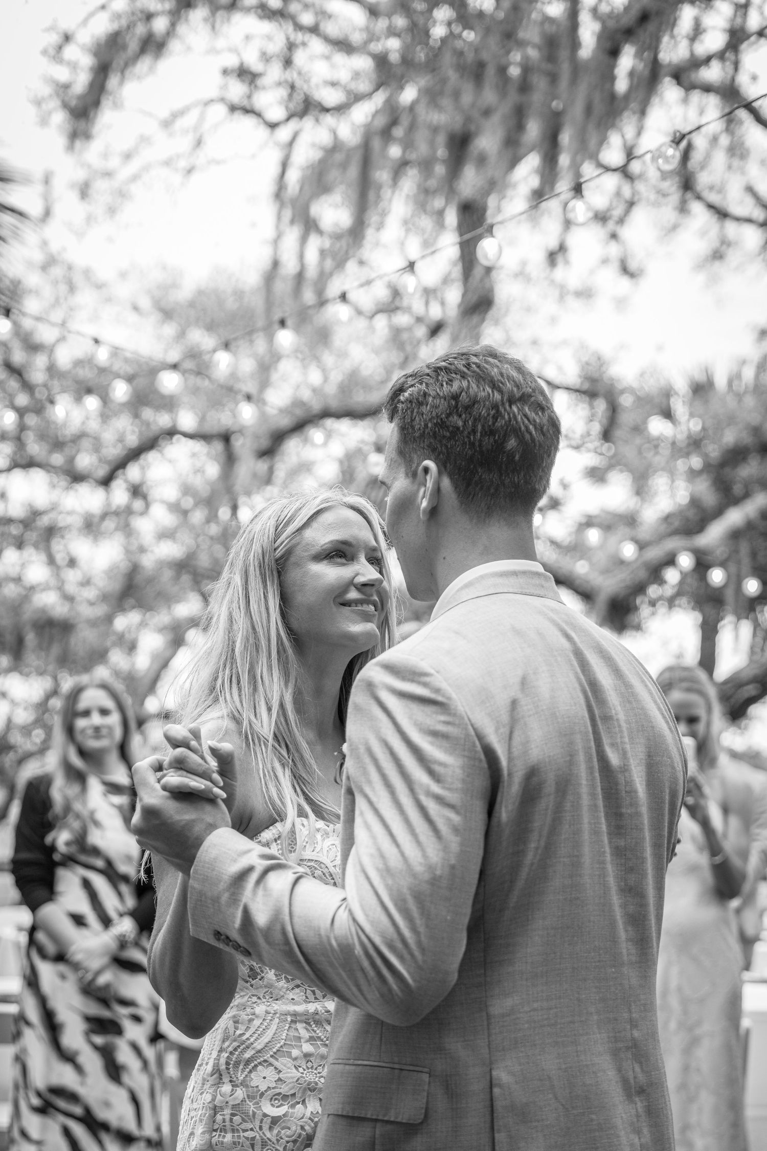 Bride and groom share an emotional first dance outdoors under Spanish moss-draped trees with string lights.