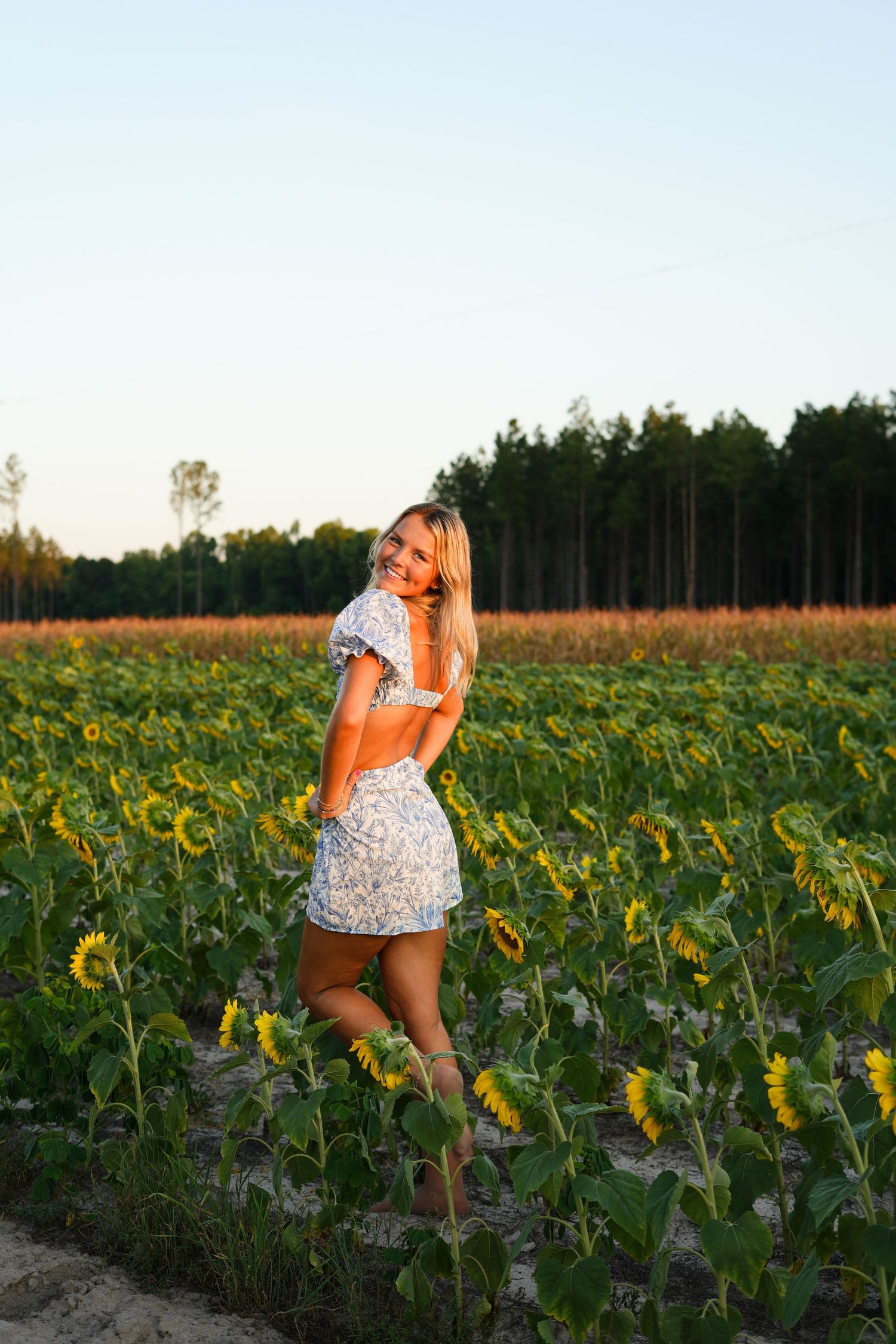 Person in a floral dress exploring a vibrant sunflower field during golden hour.