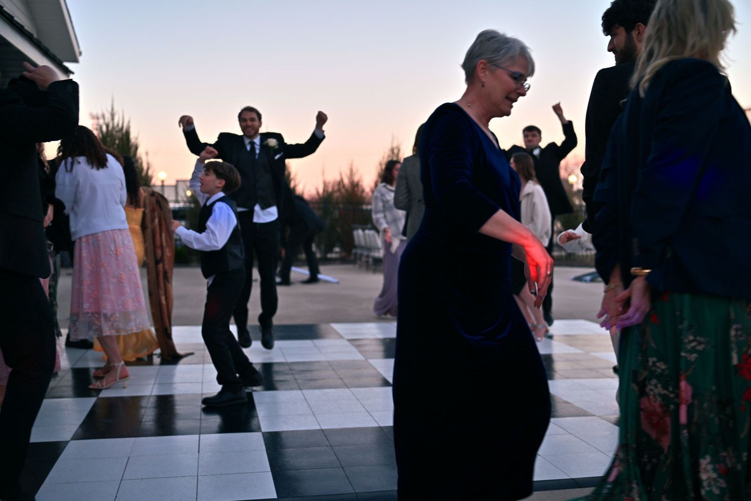 Guests dancing on checkered floor at outdoor wedding reception during sunset celebration.