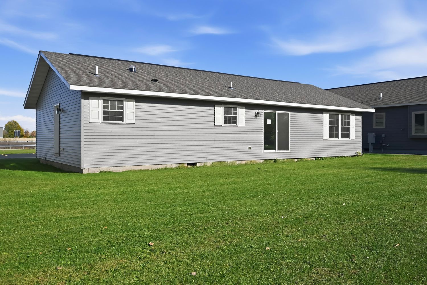 Panoramic view of a residential backyard with green lawn and gray houses in the background.