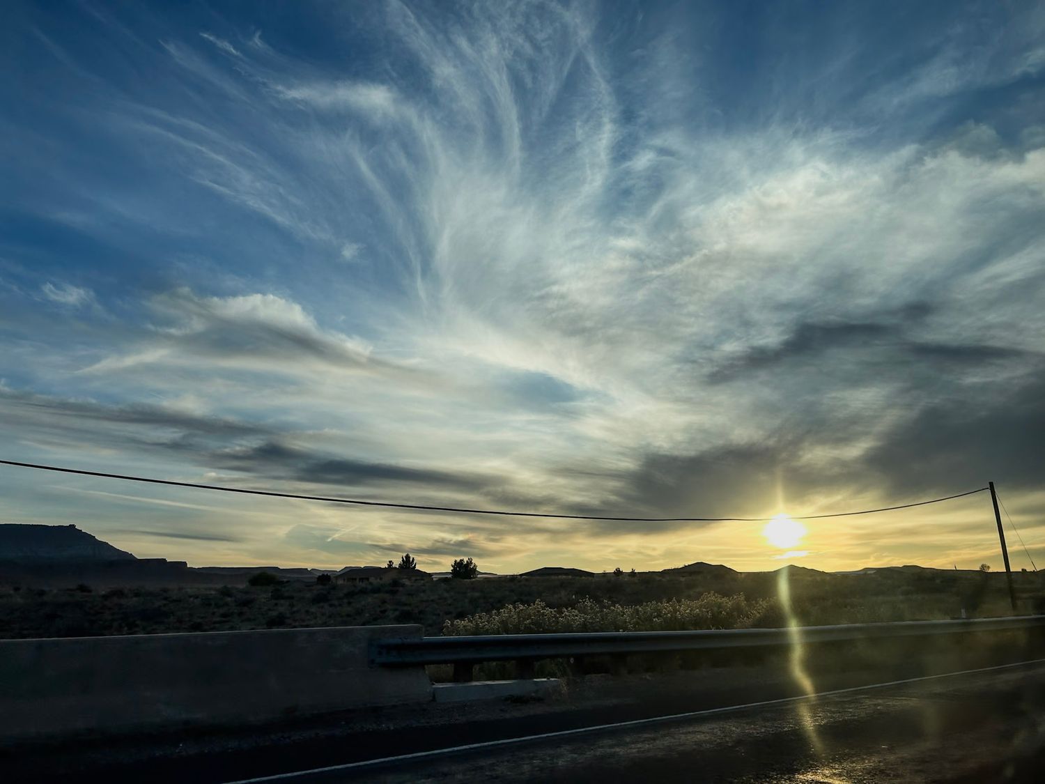 Dramatic sunset sky with wispy clouds and sun rays over mountain silhouettes.