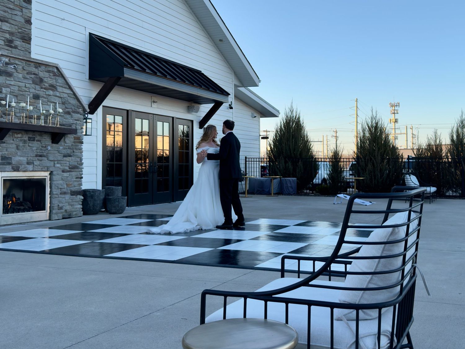 Bride and groom share a romantic moment on a black and white checkered outdoor dance floor at sunset.